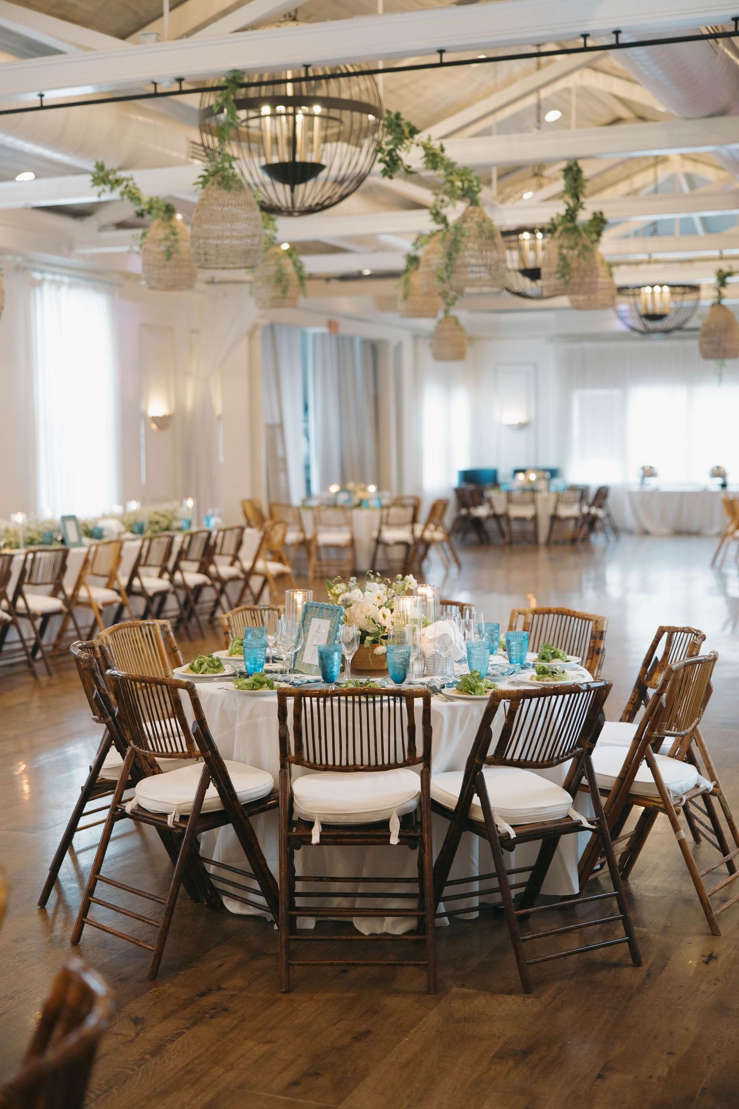 Rustic wedding reception venue with wooden chairs and round tables under exposed beam ceiling.