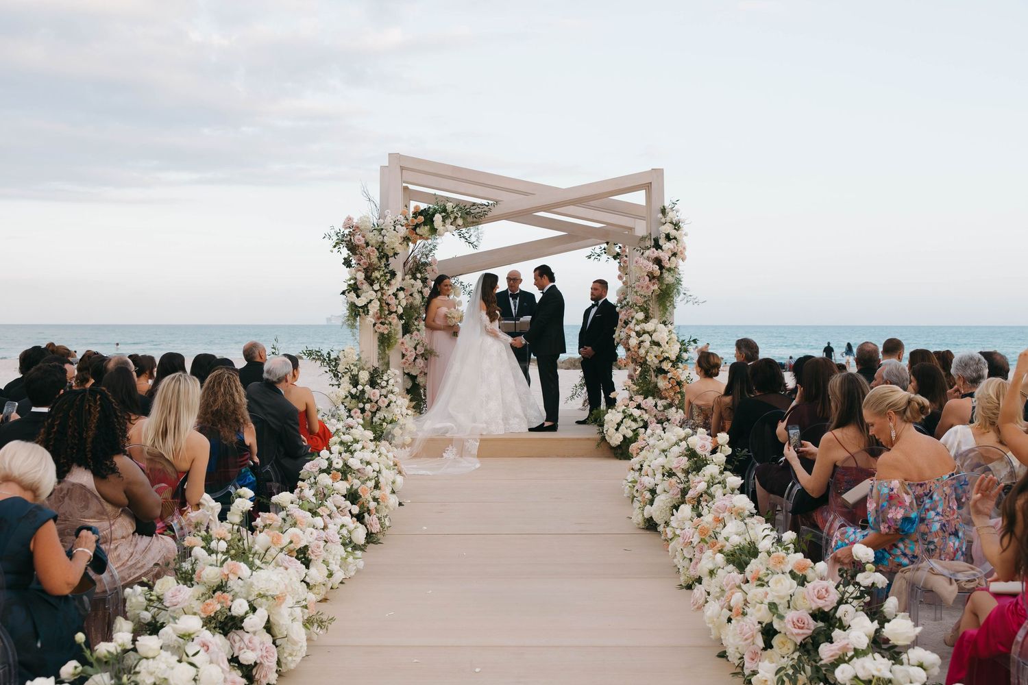 Elegant beach wedding setup with white floral arch and guests seated on either side.