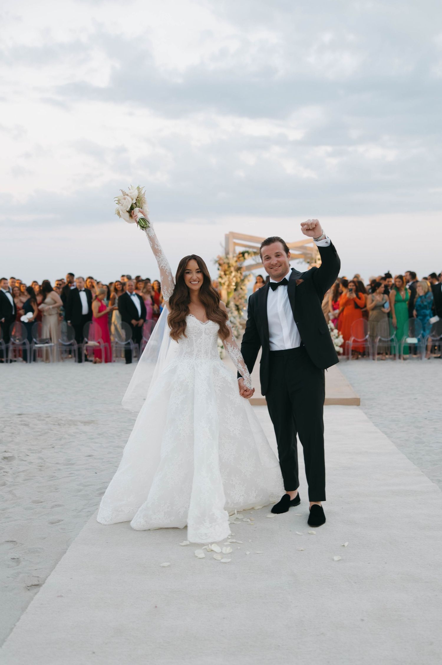 A joyful wedding celebration unfolds on a pristine beach with guests watching the newlyweds.