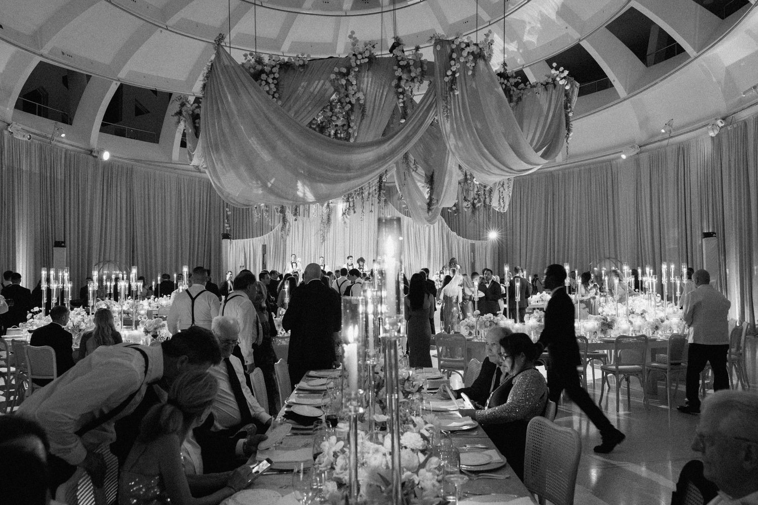 Wide angle view of an elegant wedding reception venue with white draping and chandeliers.