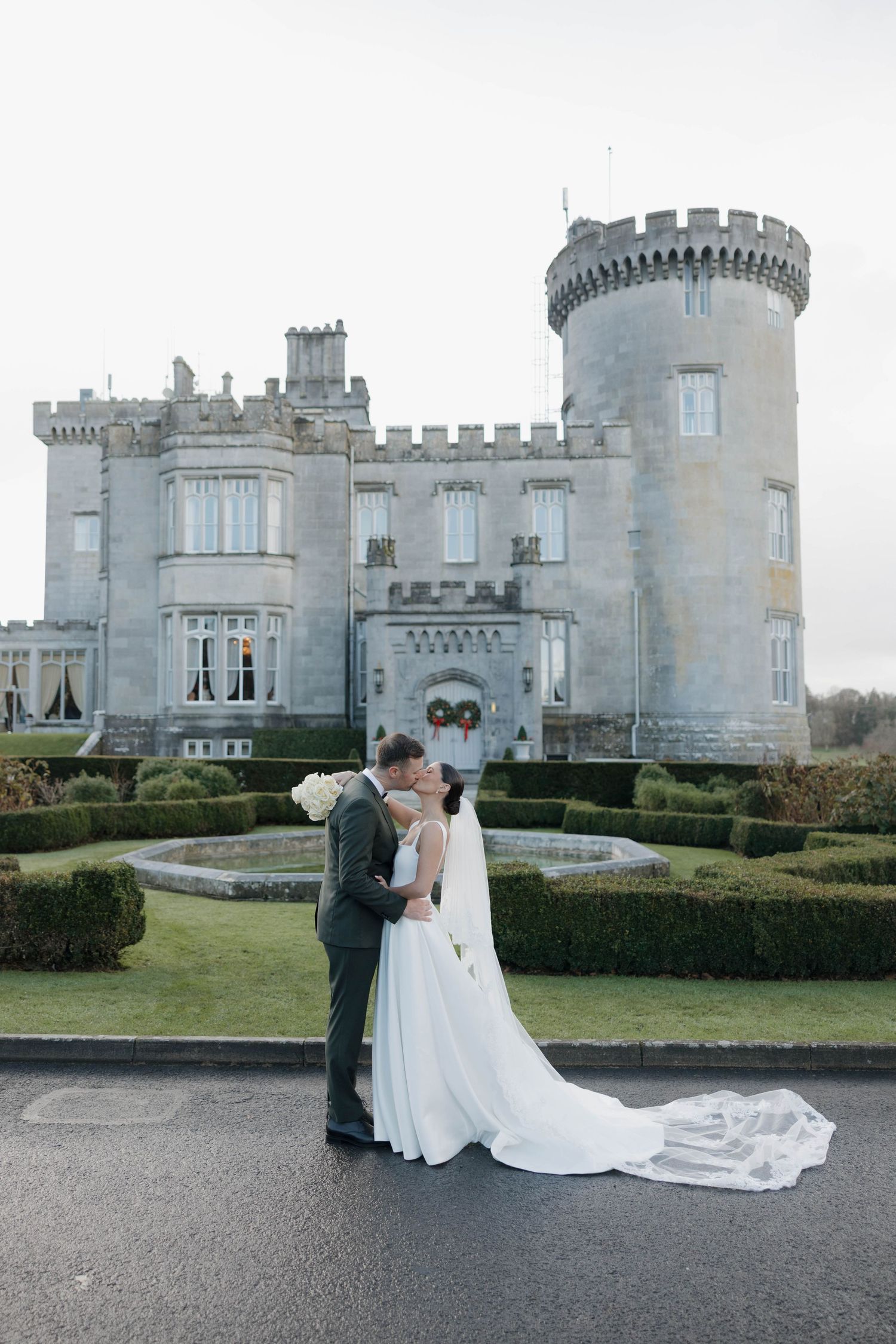Romantic wedding photos taken in front of a majestic stone castle with turrets and landscaped grounds.