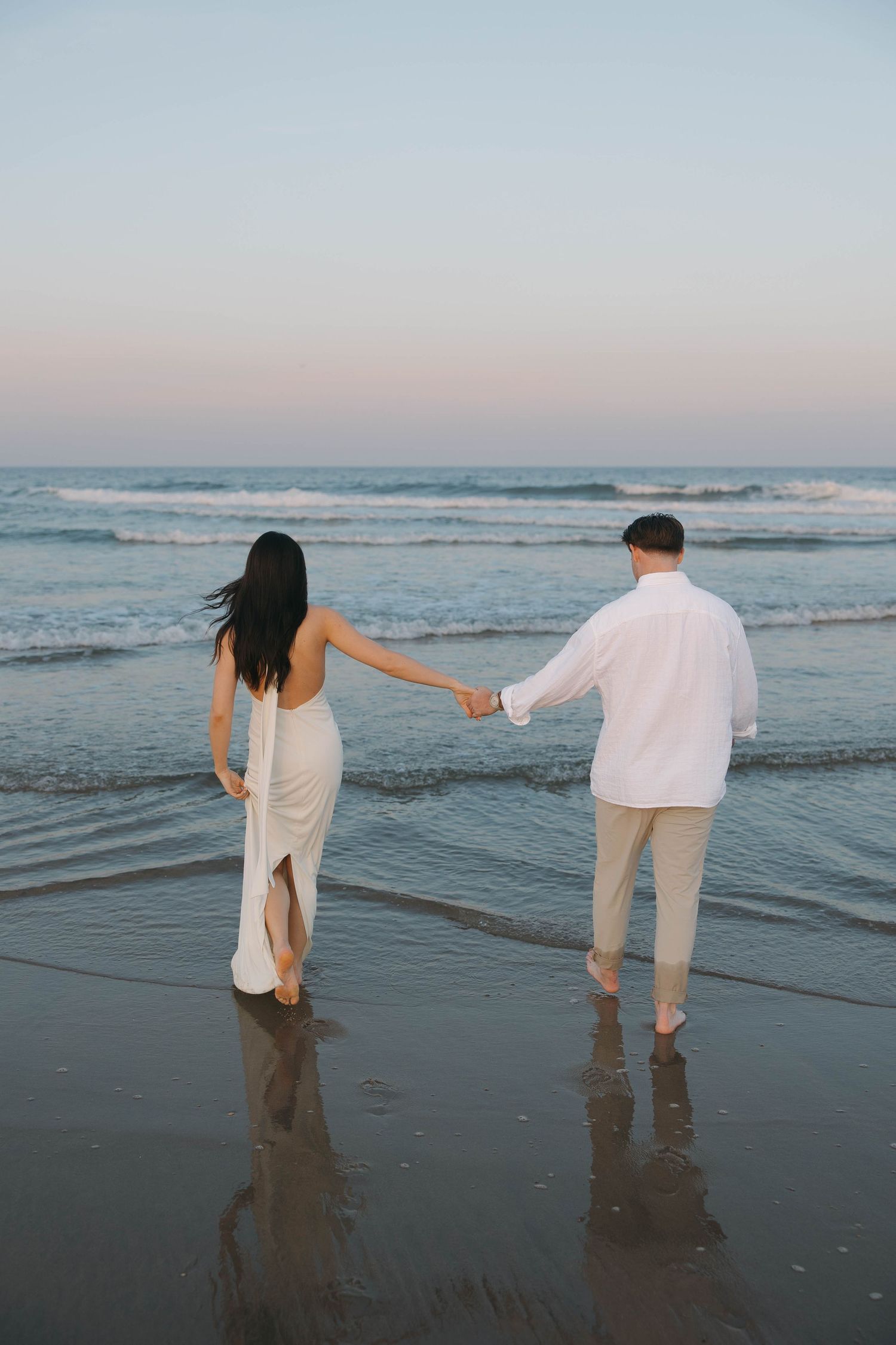Couple walking hand in hand along the beach at sunset creating romantic silhouettes.