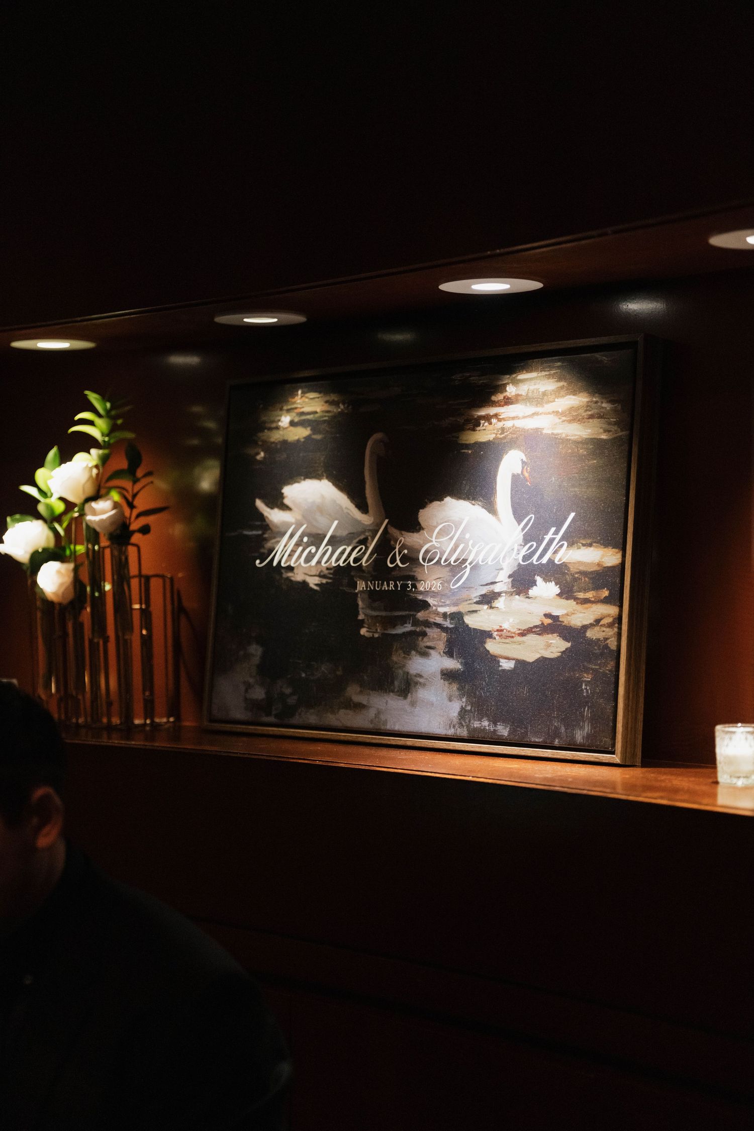Elegant wedding signage with swan design illuminated in dark ambiance.