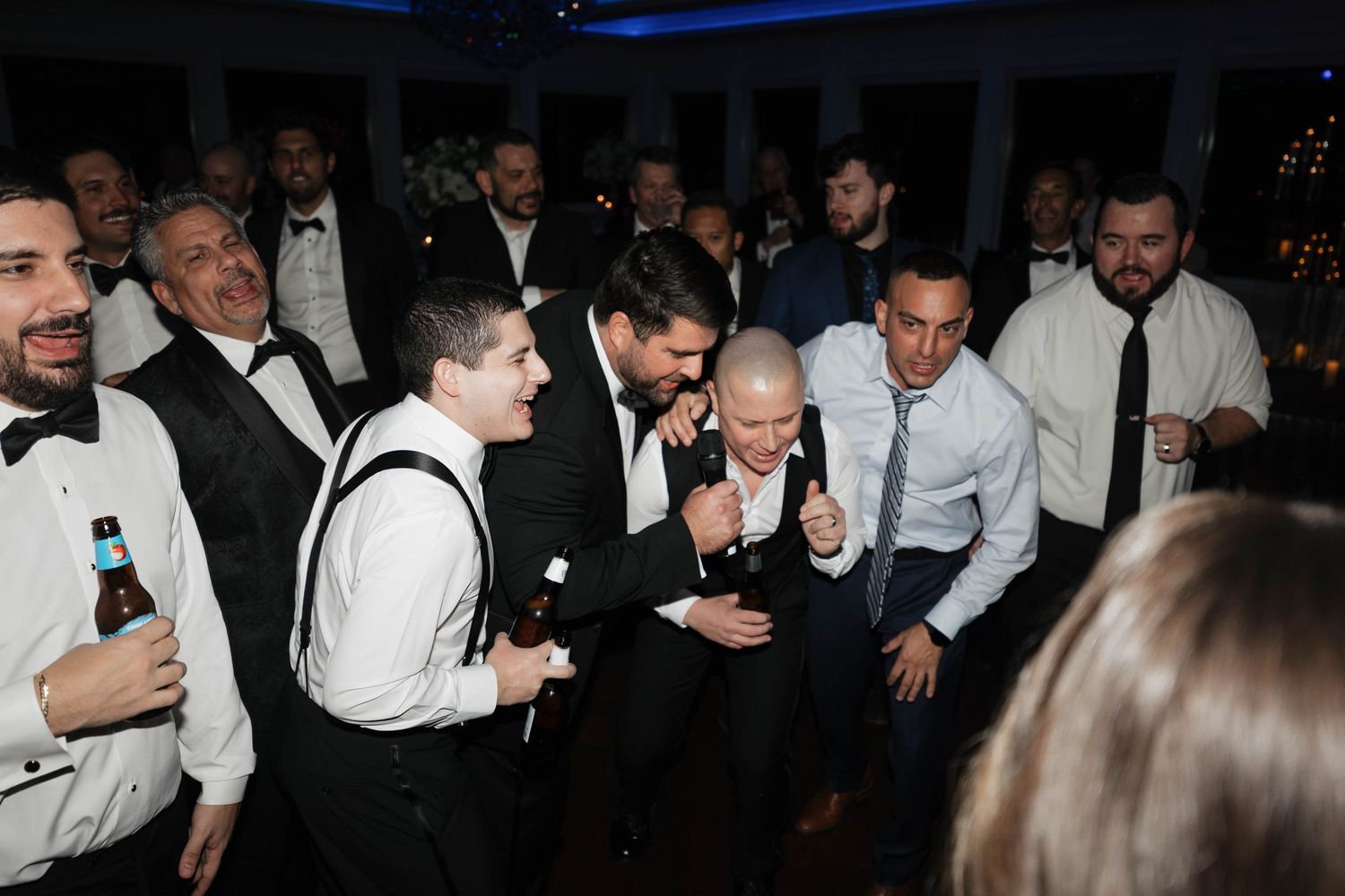 Wedding reception guests dance and celebrate on a crowded dance floor under blue lighting.
