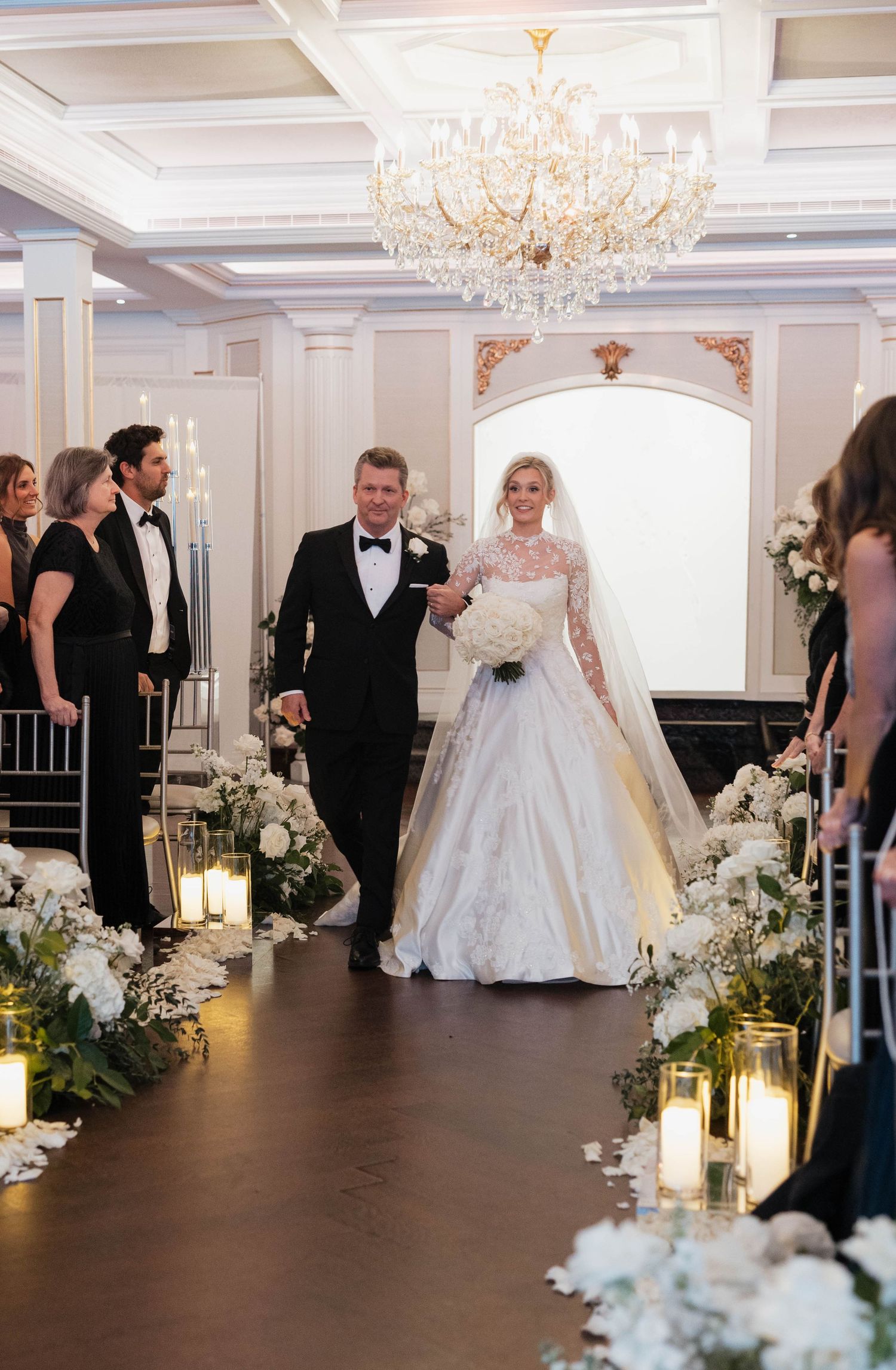 Wedding ceremony in a luxurious ballroom with crystal chandeliers and white floral decorations.
