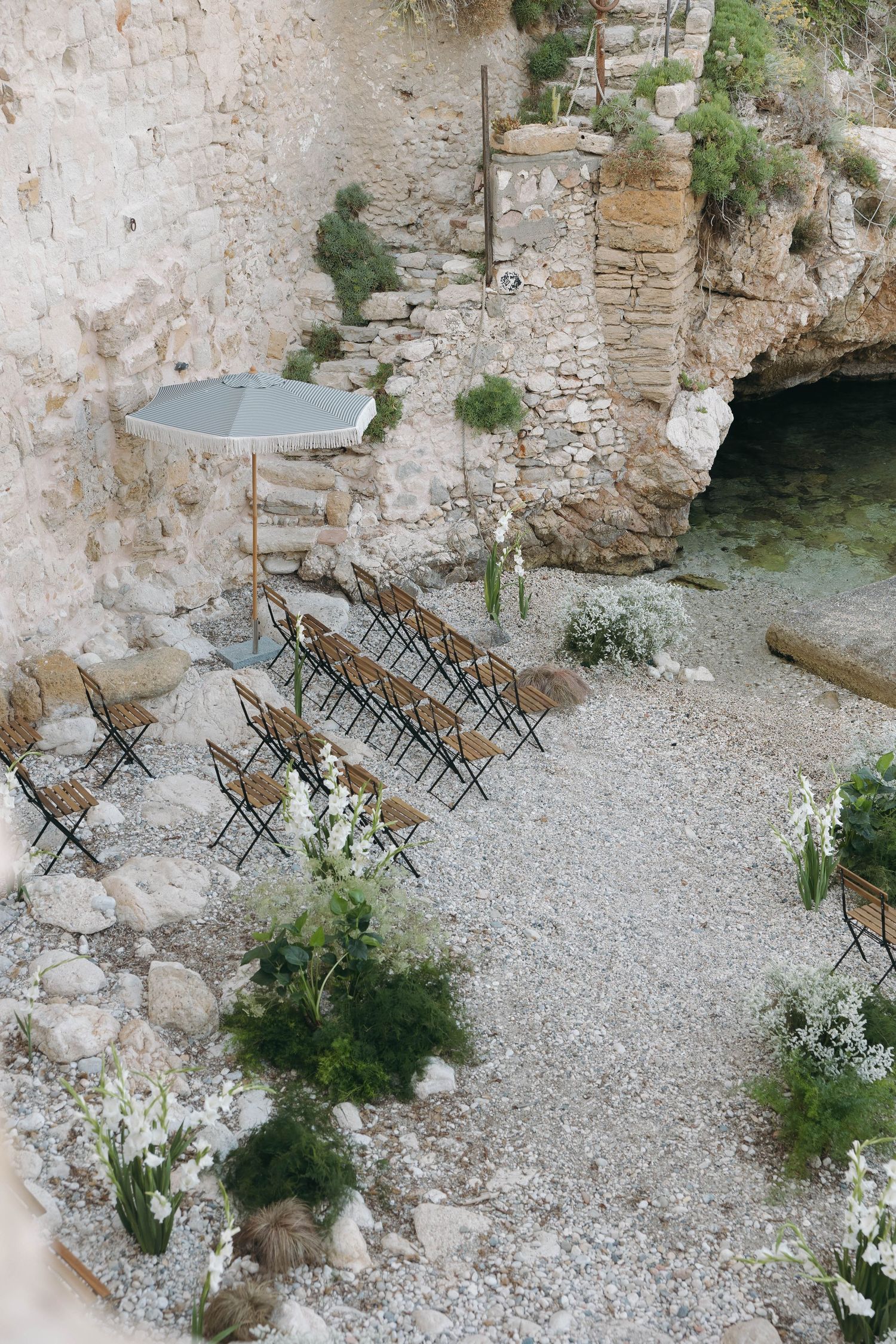 Rustic wedding ceremony space on a pebble beach surrounded by dramatic limestone cliffs.