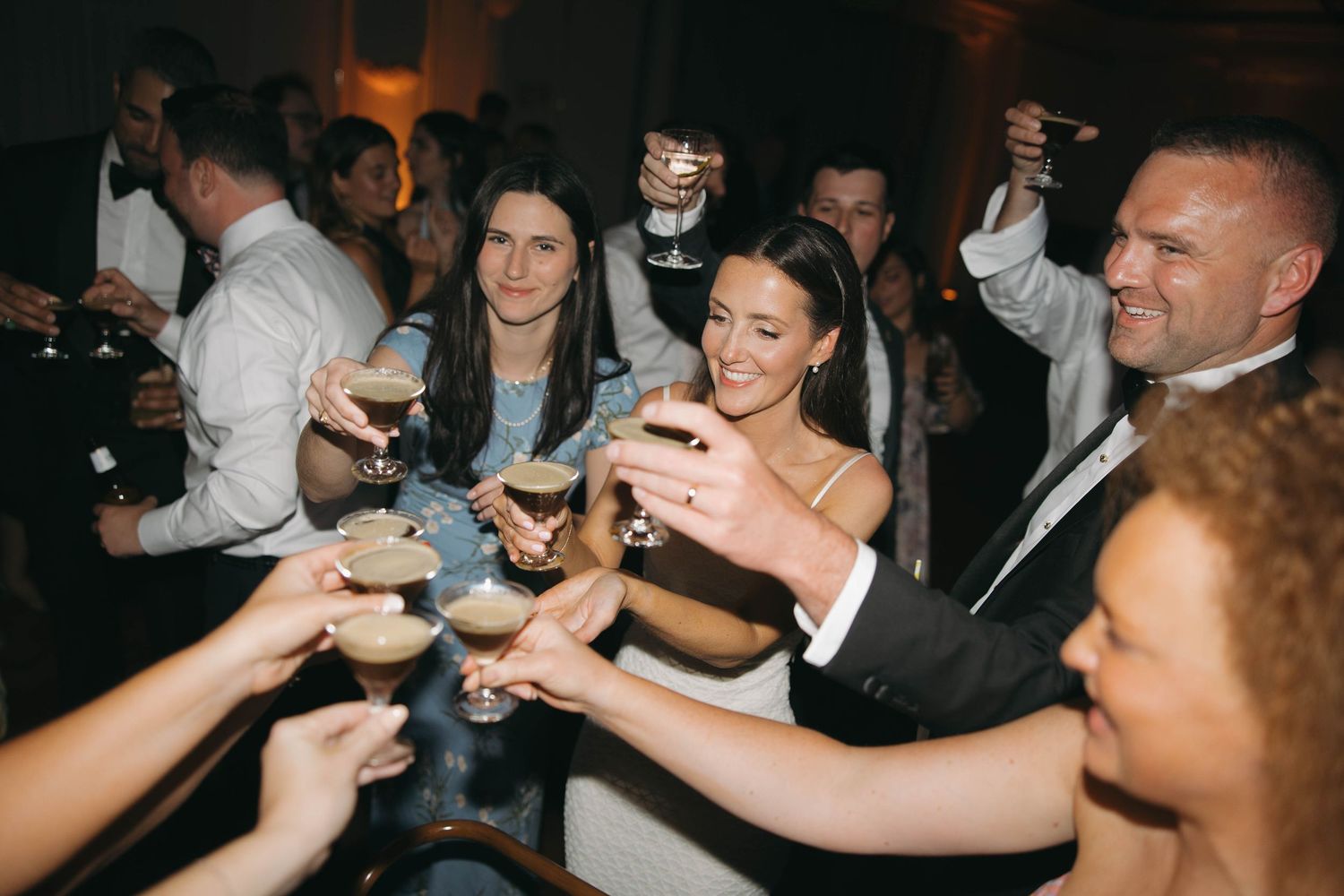 Wedding reception guests dancing and celebrating on a dark dance floor.