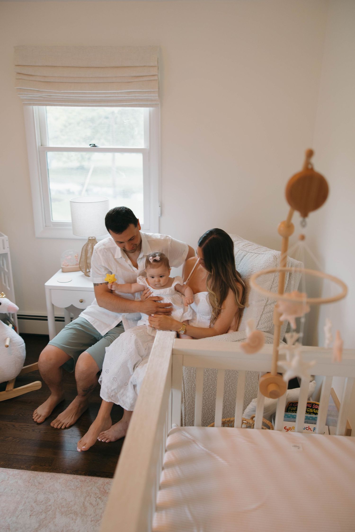 Family spending intimate moments together on a white bed in a bright, minimalist bedroom.