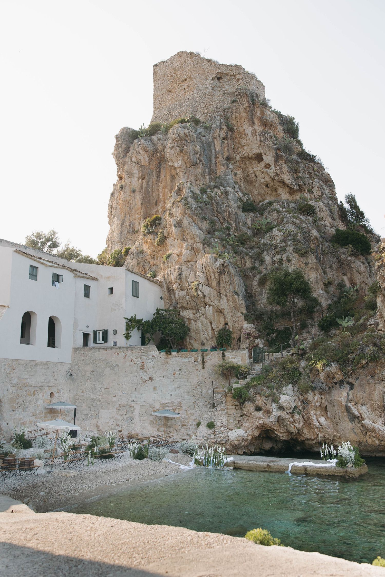 Historic white buildings built into limestone cliffs overlooking turquoise Mediterranean waters.