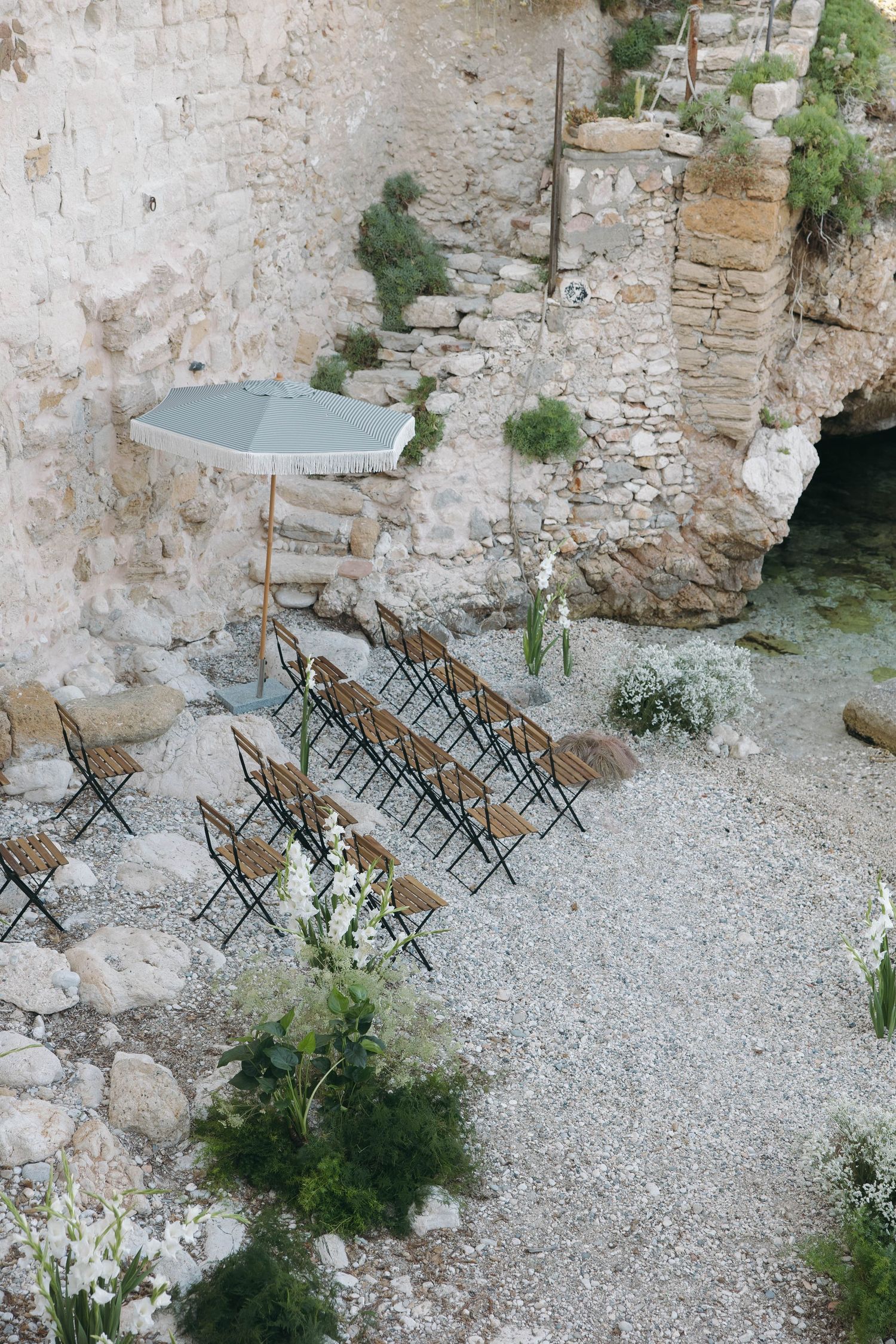 Folding chairs arranged in rows on a gravel surface against ancient stone walls in an outdoor venue.
