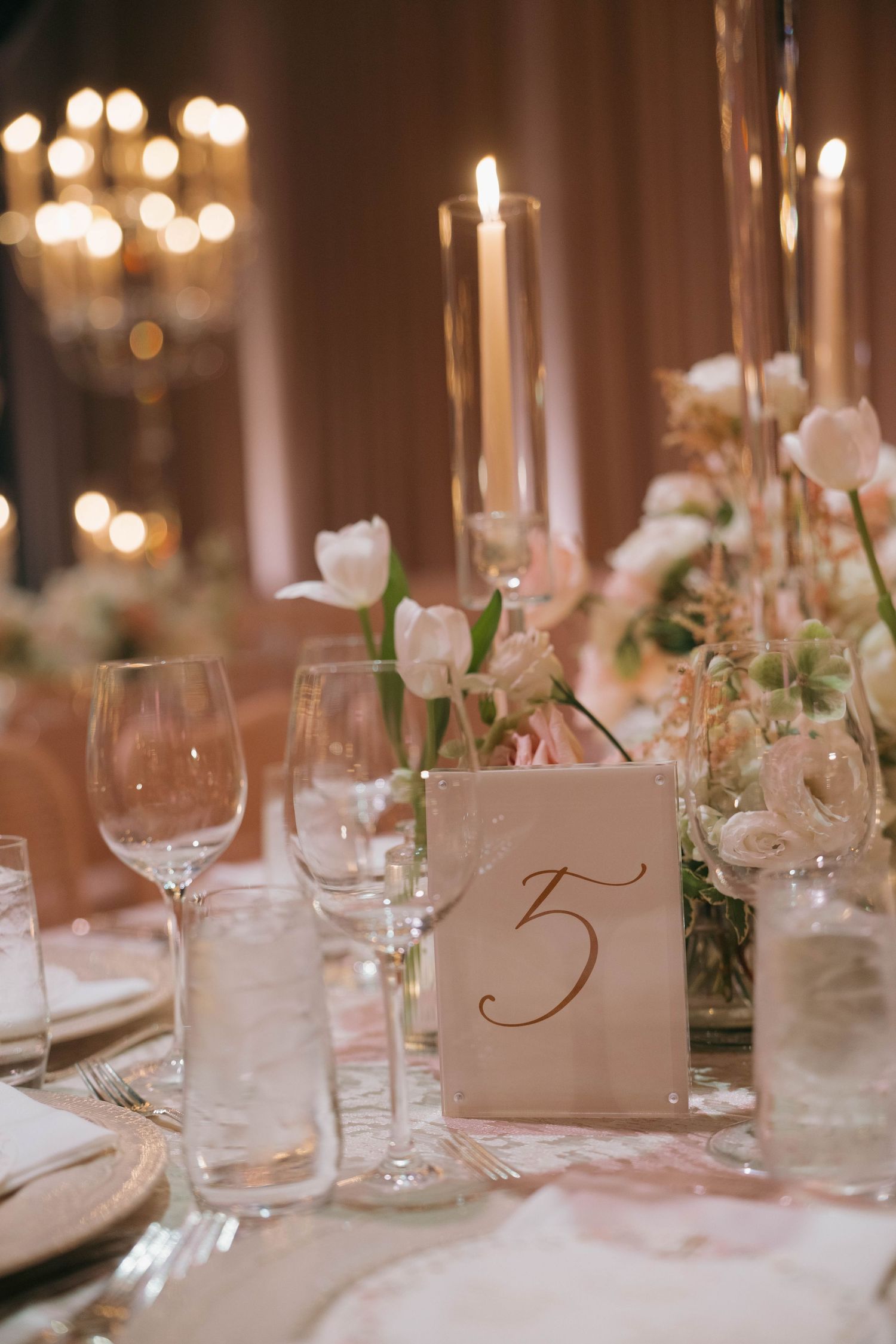 Wedding table settings with numbered place cards, crystal glassware, and floral centerpieces.