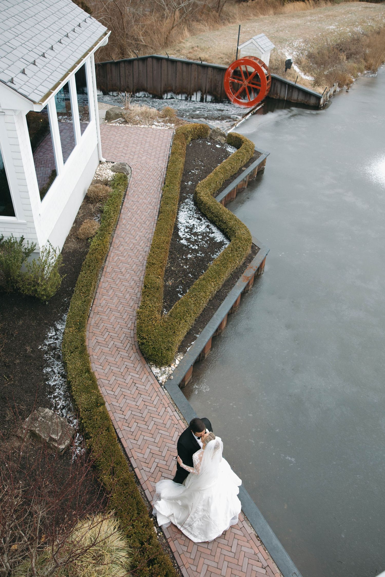 Aerial view of a couple on a brick pathway next to water with a red waterwheel in background.