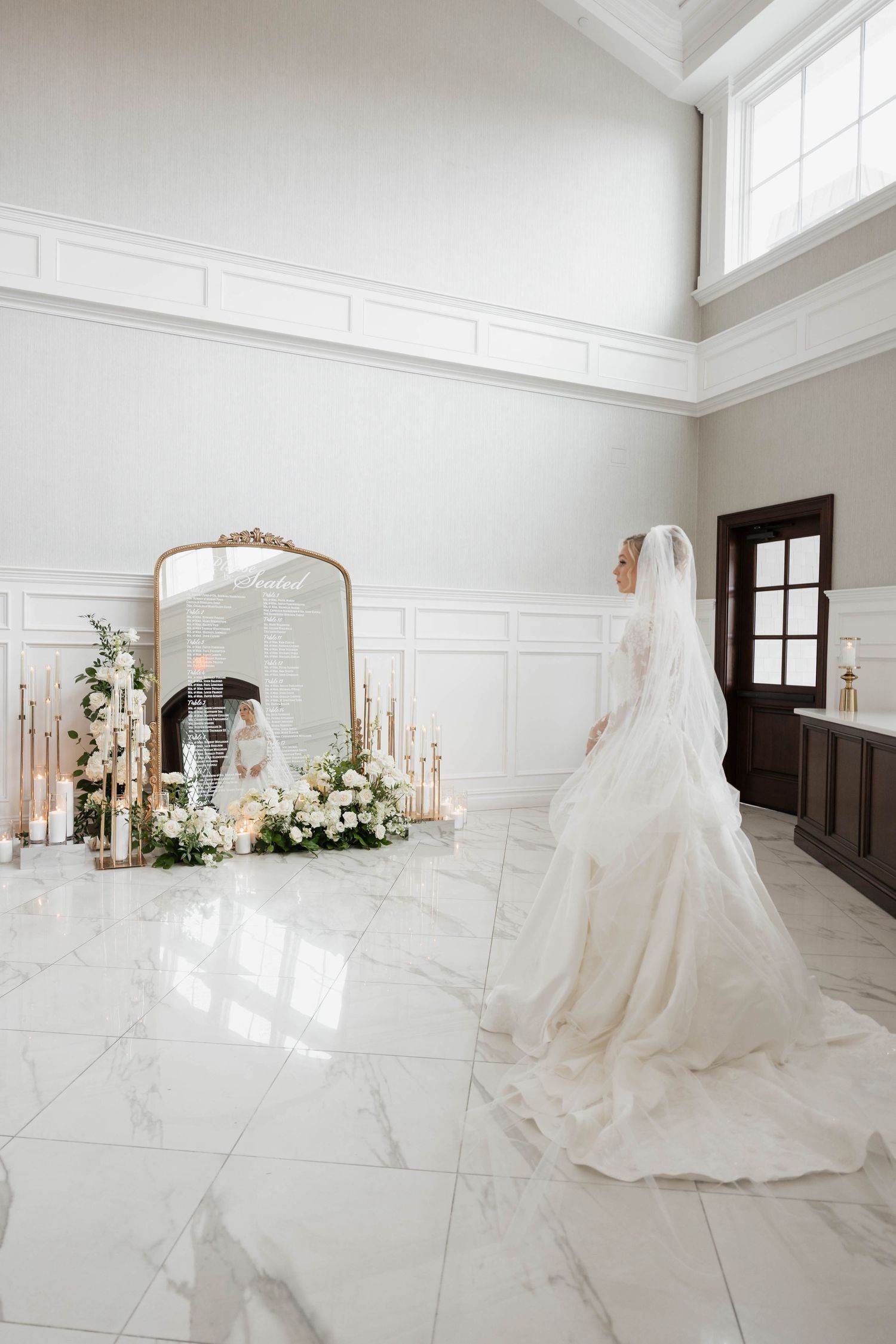 Wedding dress showcased in a bright white room with marble floors and floral arrangements.