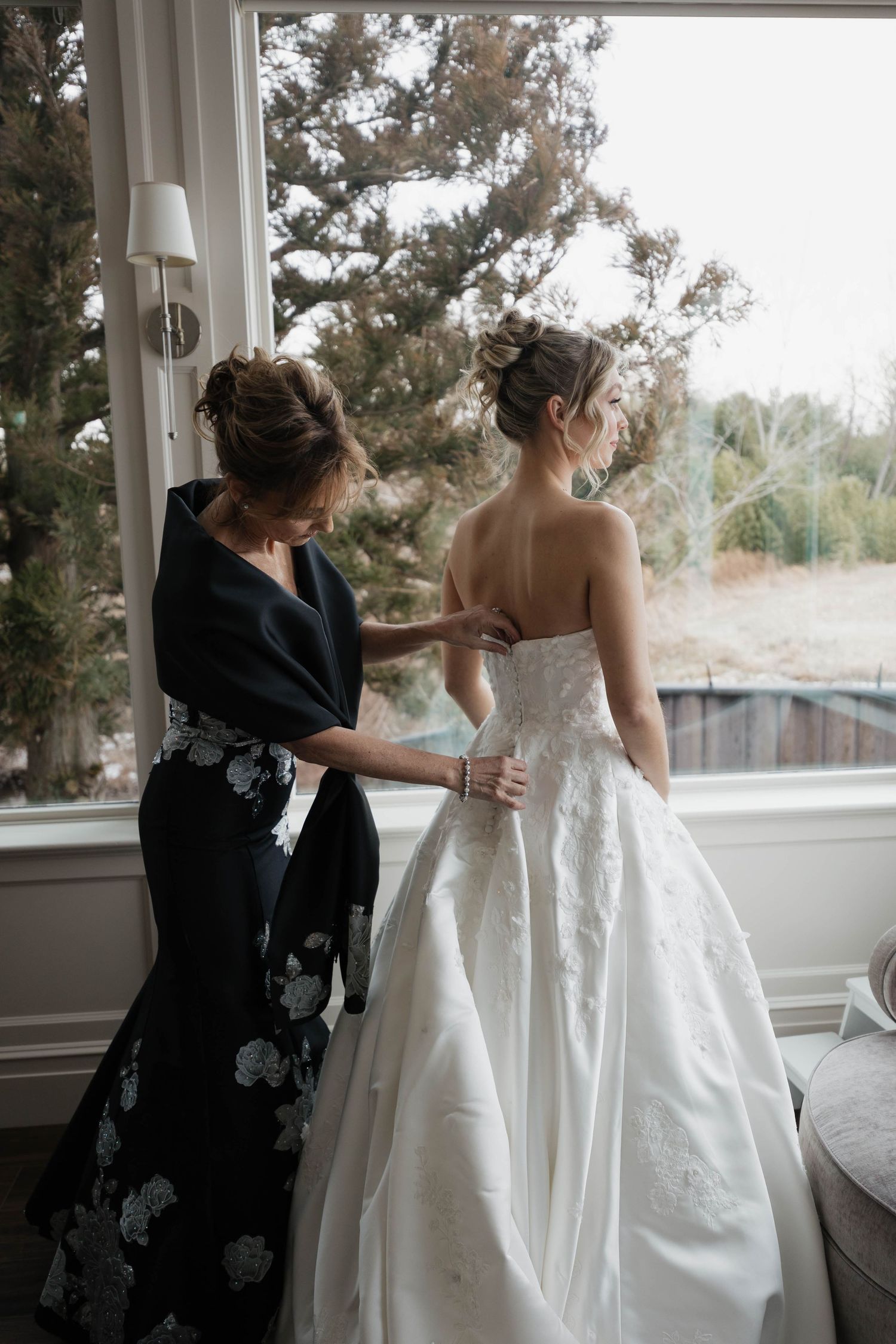 Wedding dress preparation scene with floral dress detail by large window.