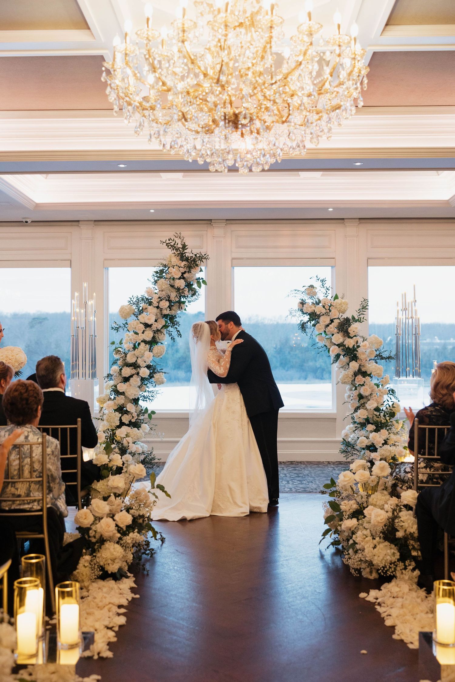 Wedding ceremony space with crystal chandelier and white floral arches creating romantic atmosphere.