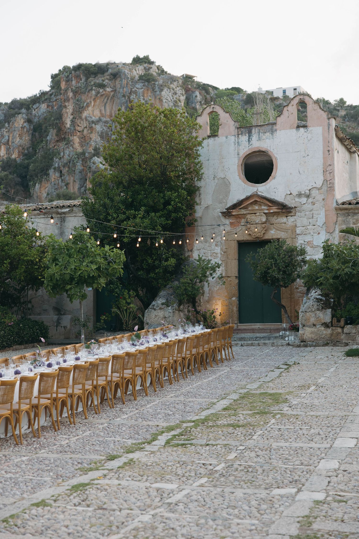 Long rows of wooden chairs set up for outdoor event in front of historic stone building.