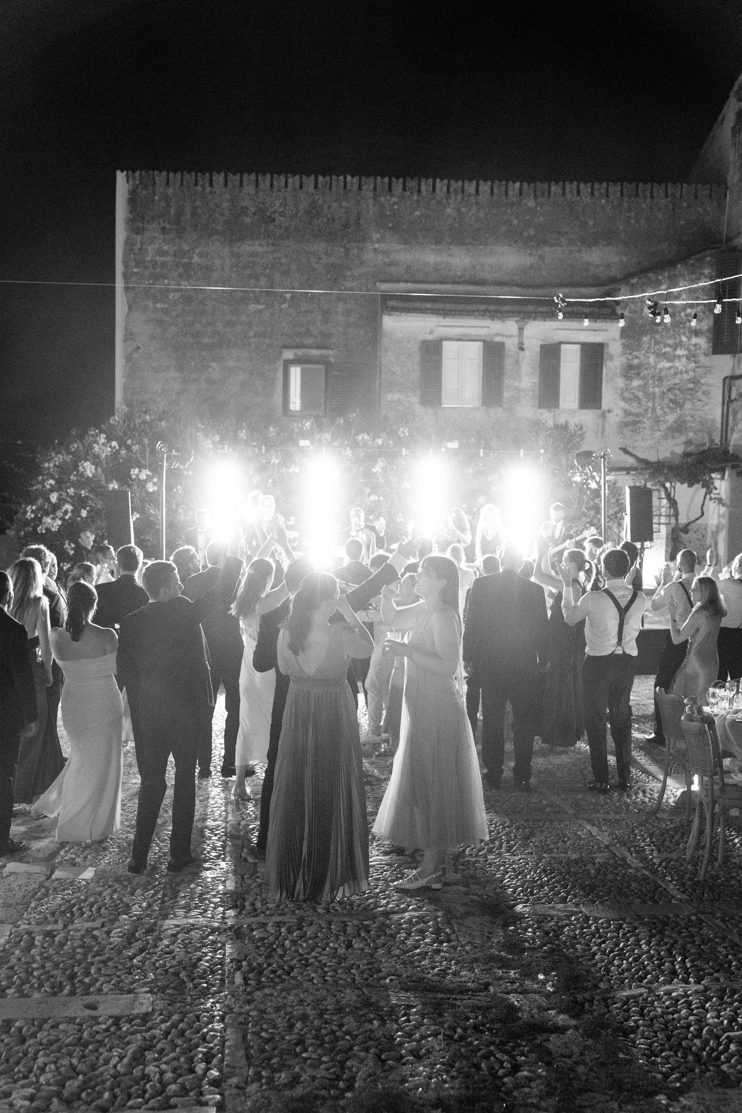 Evening celebration with bright lights illuminating guests against historic stone walls.
