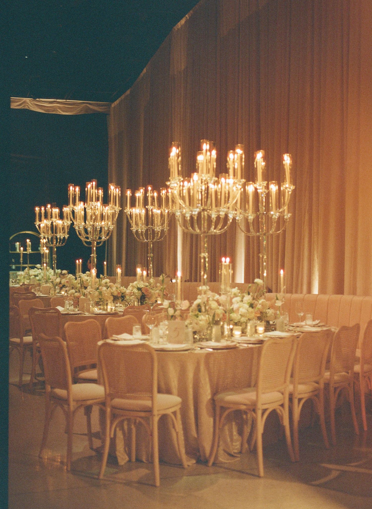Elegant wedding reception tables set with tall candelabras and floral centerpieces in a dimly lit banquet hall.