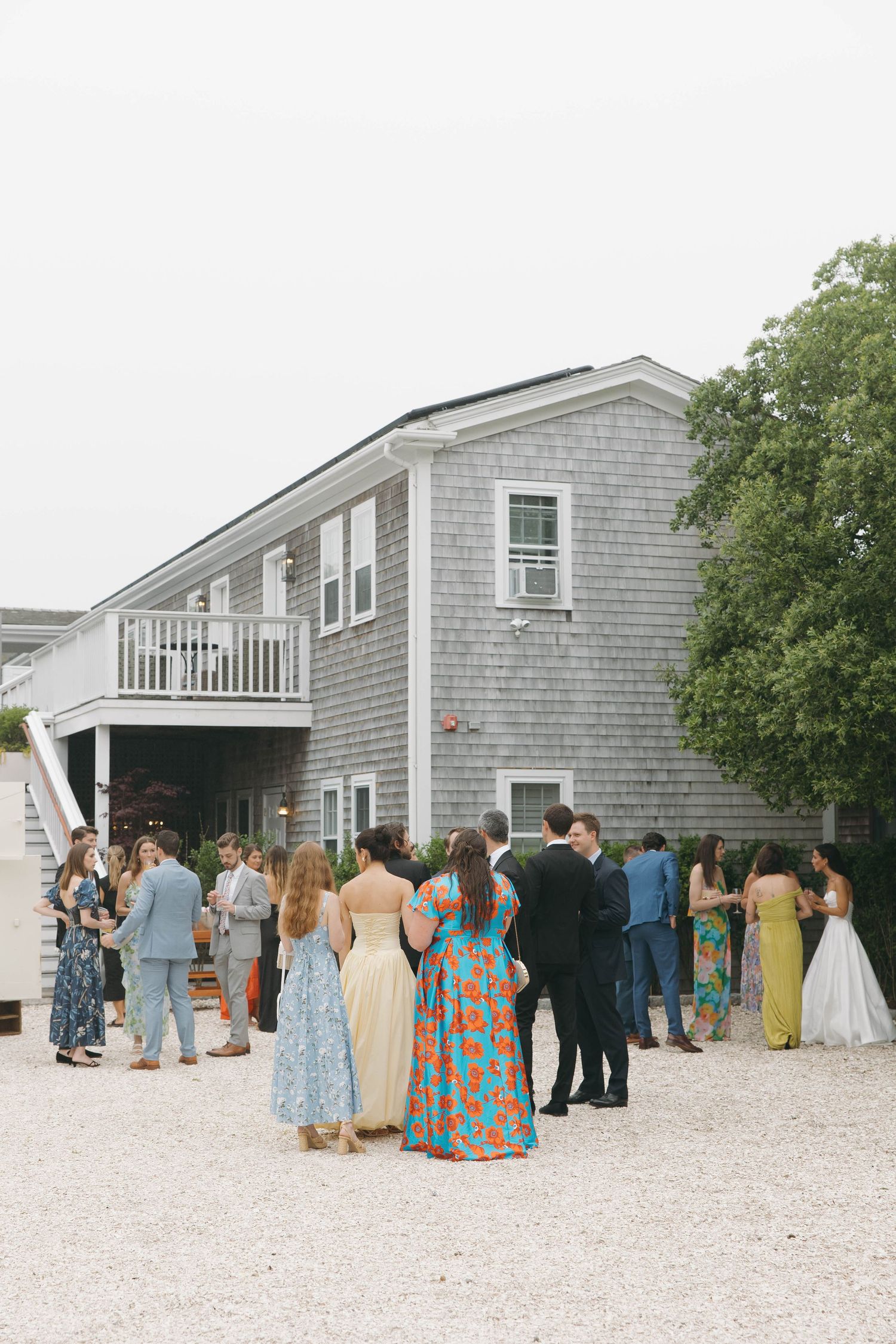 Wedding celebration outside a coastal gray shingled building with guests in formal attire.