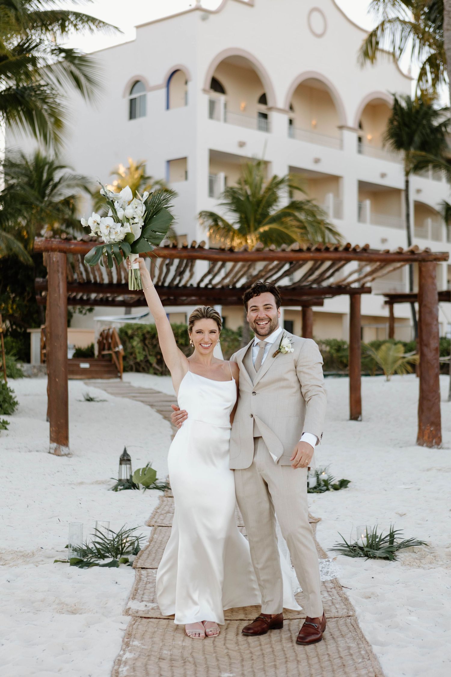 Joyful wedding couple celebrating under wooden pergola at tropical beach resort.