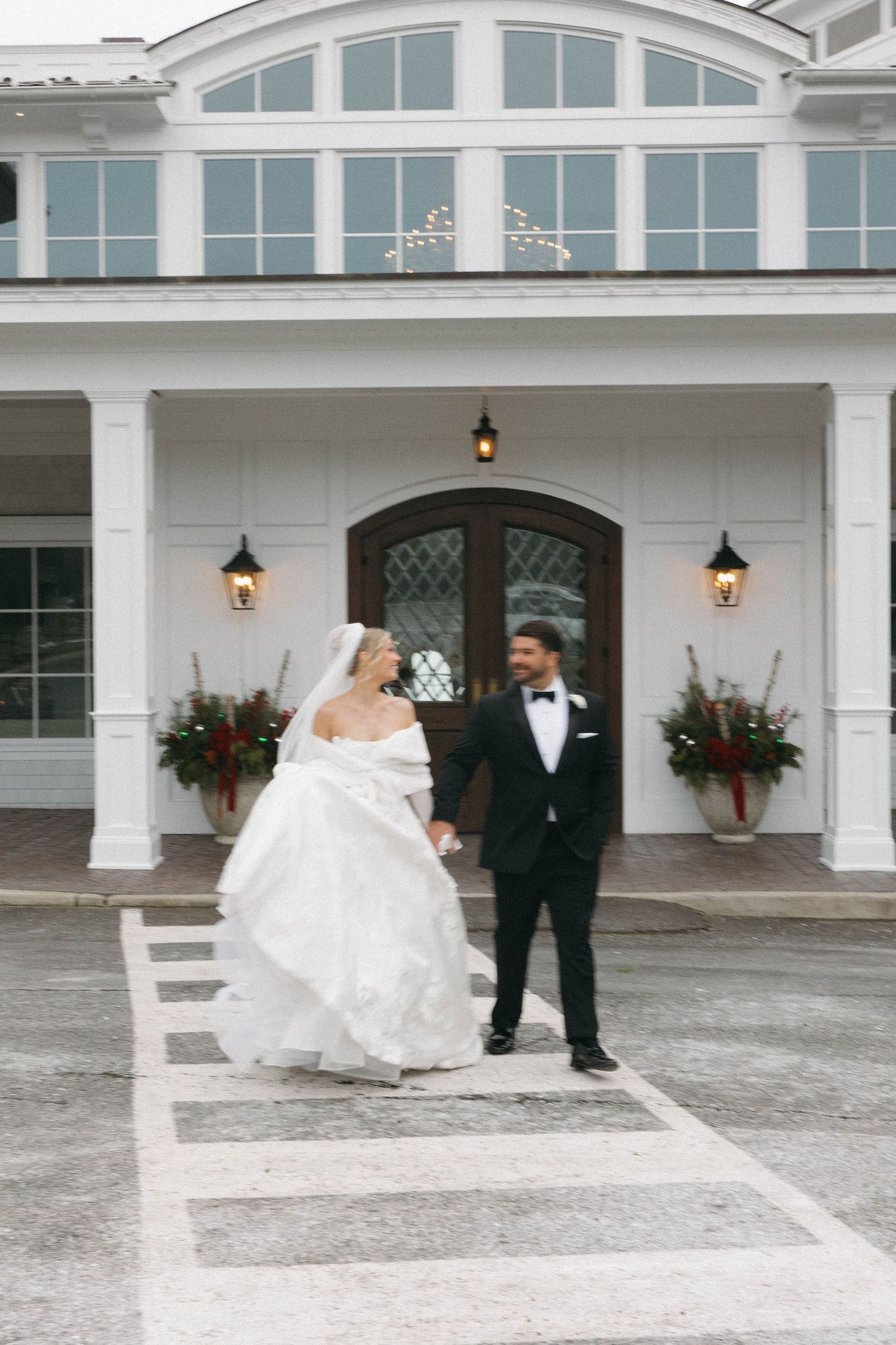 An elegant wedding scene unfolds in front of a white colonial building with hanging lanterns.