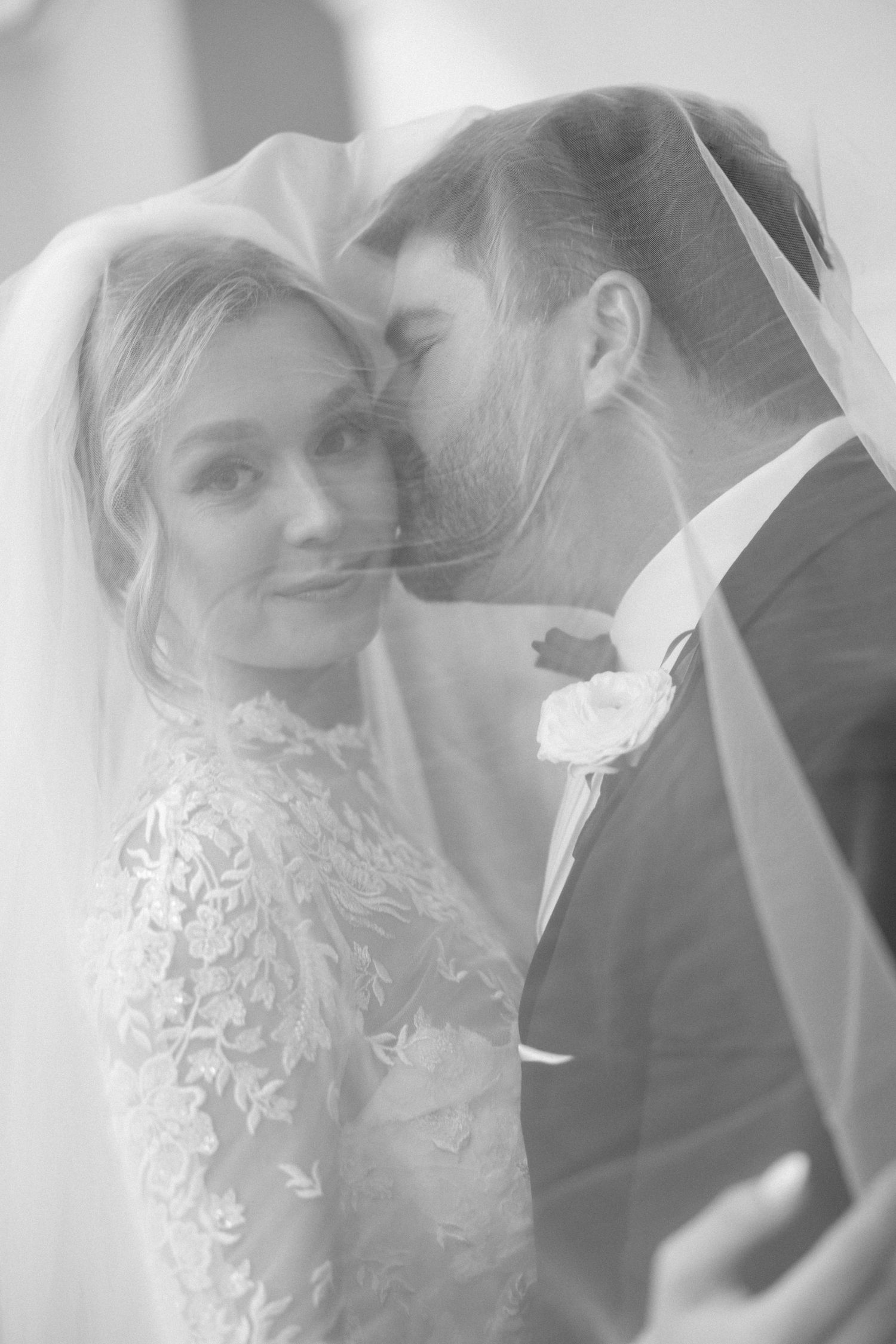 Romantic wedding portrait through sheer veil in soft, dreamy lighting.