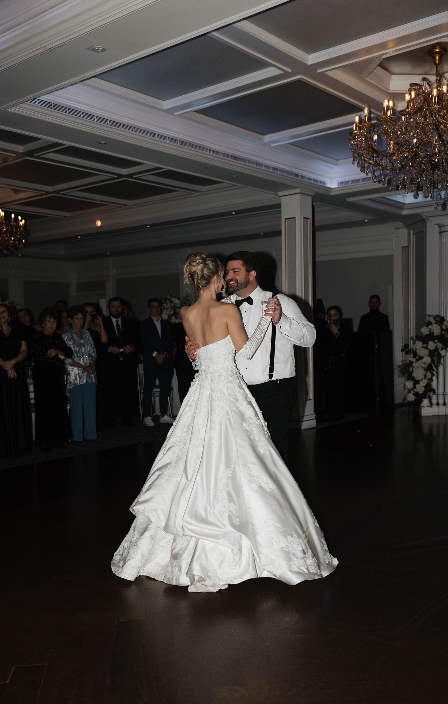 A couple performs an elegant dance lift during their first dance at a wedding reception in an elegant ballroom.