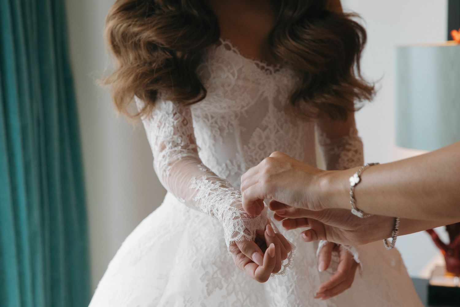 Close-up details of a bride's white lace wedding dress being adjusted.