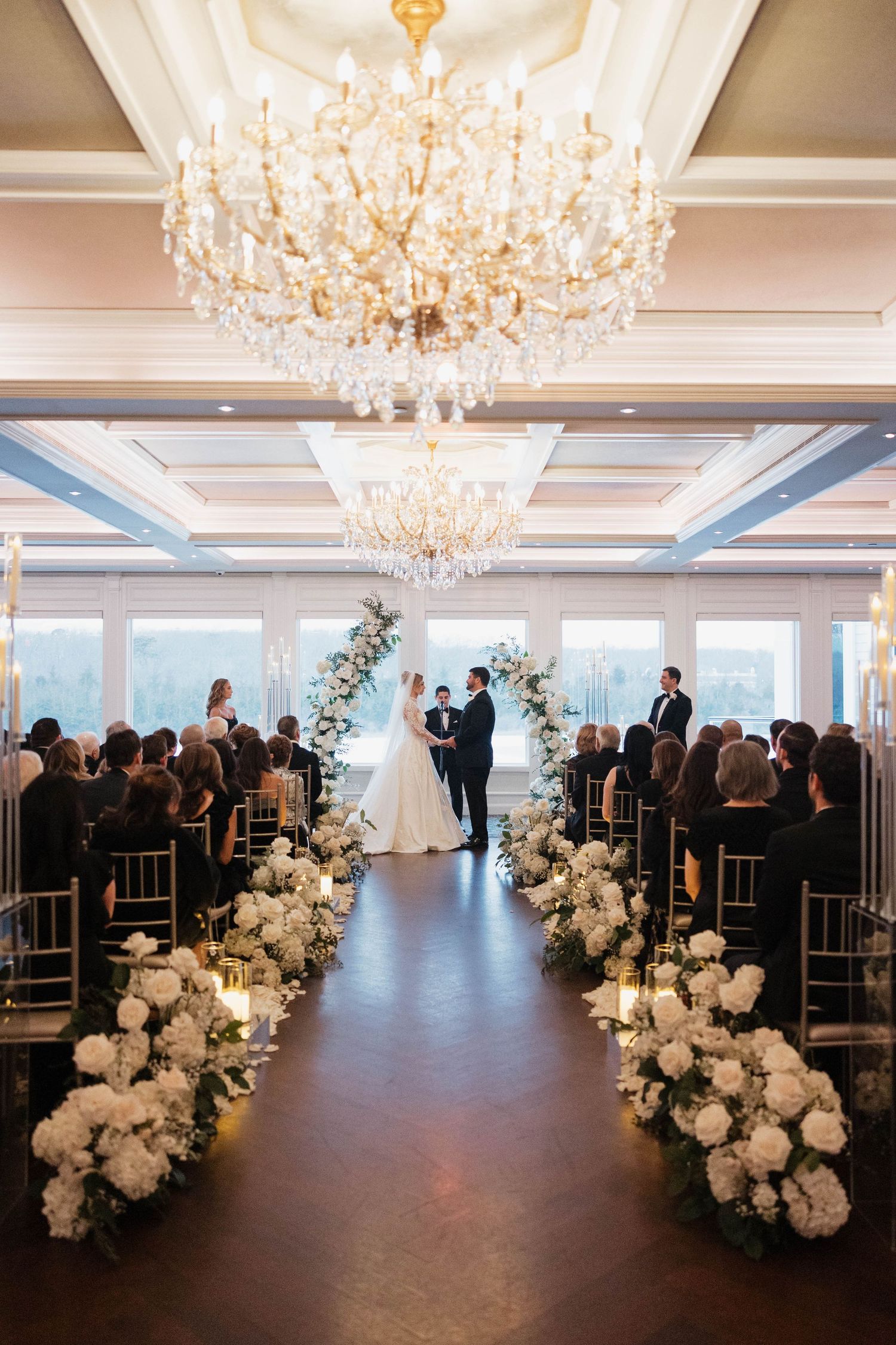 Wedding ceremony space with dramatic floral arrangements and crystal chandeliers in a grand ballroom.