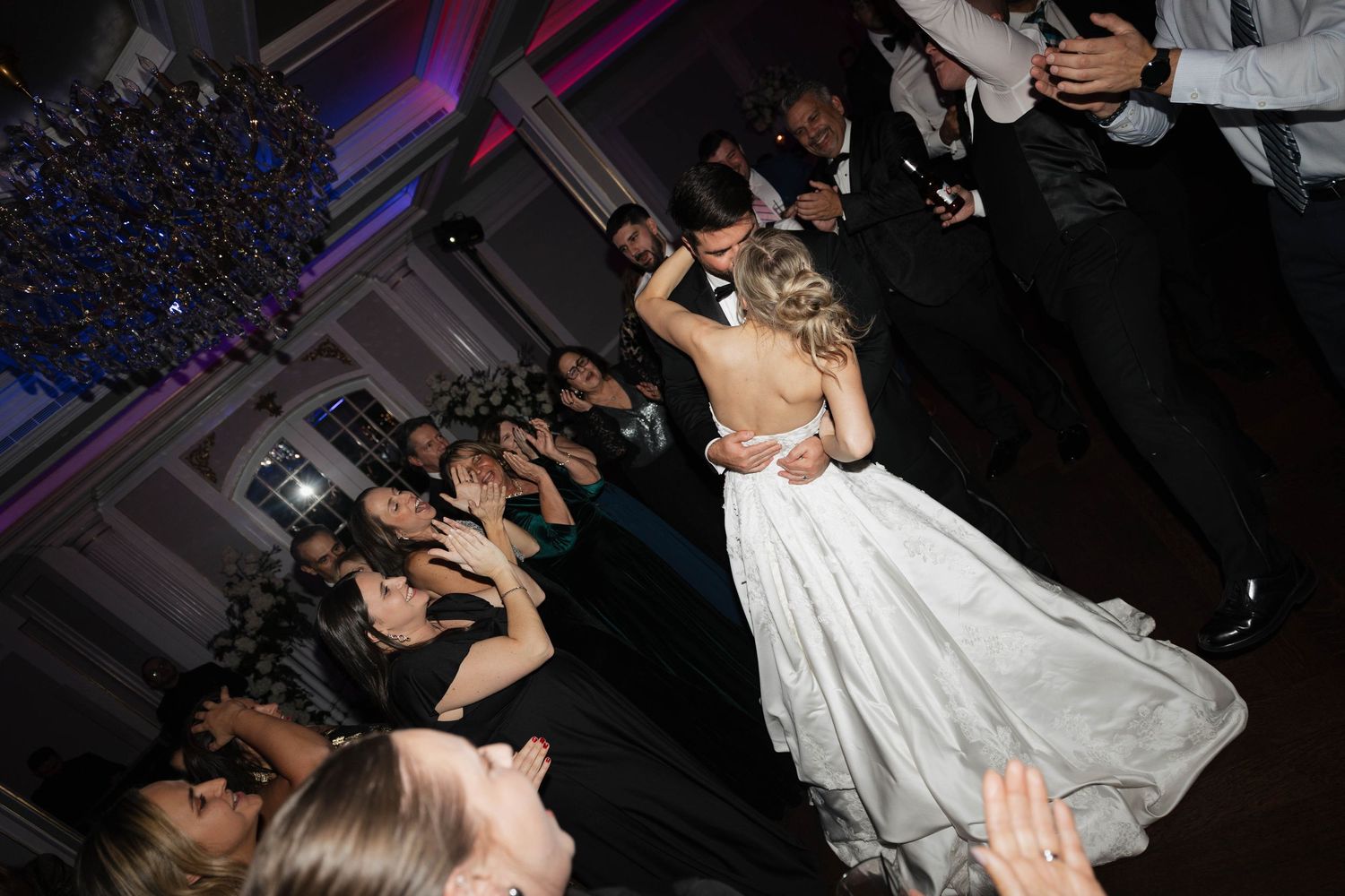 Guests dance enthusiastically at wedding reception under dramatic mood lighting.