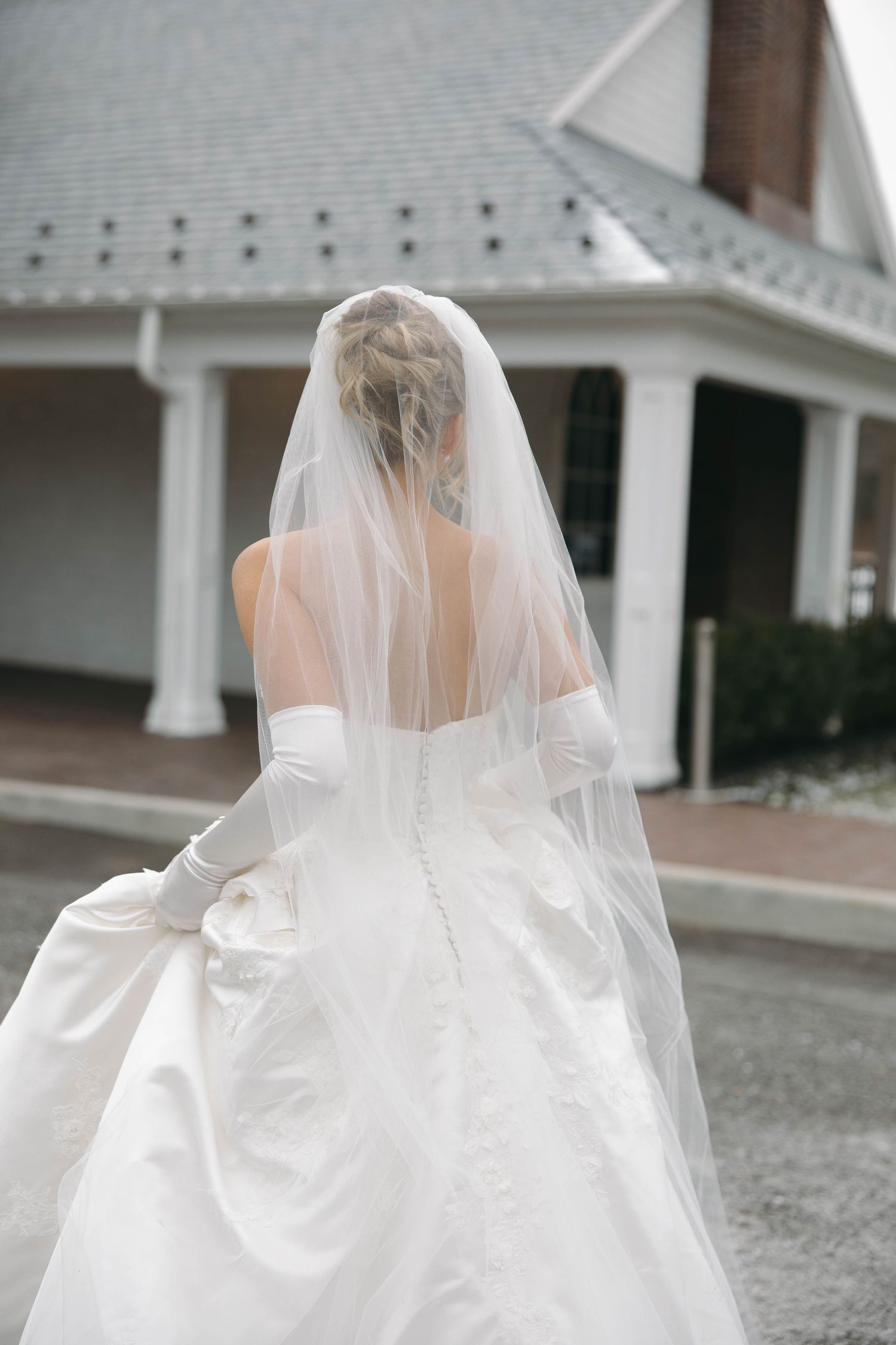 A close-up view of a flowing white wedding dress and veil from behind.