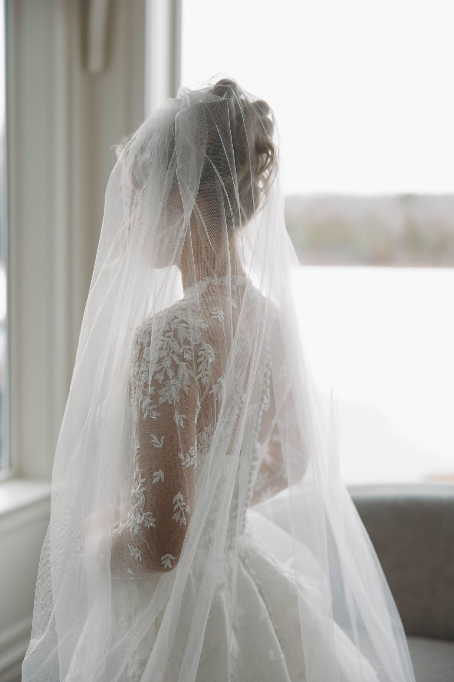 Dreamy bridal portrait with sheer veil creating romantic silhouette against window light.