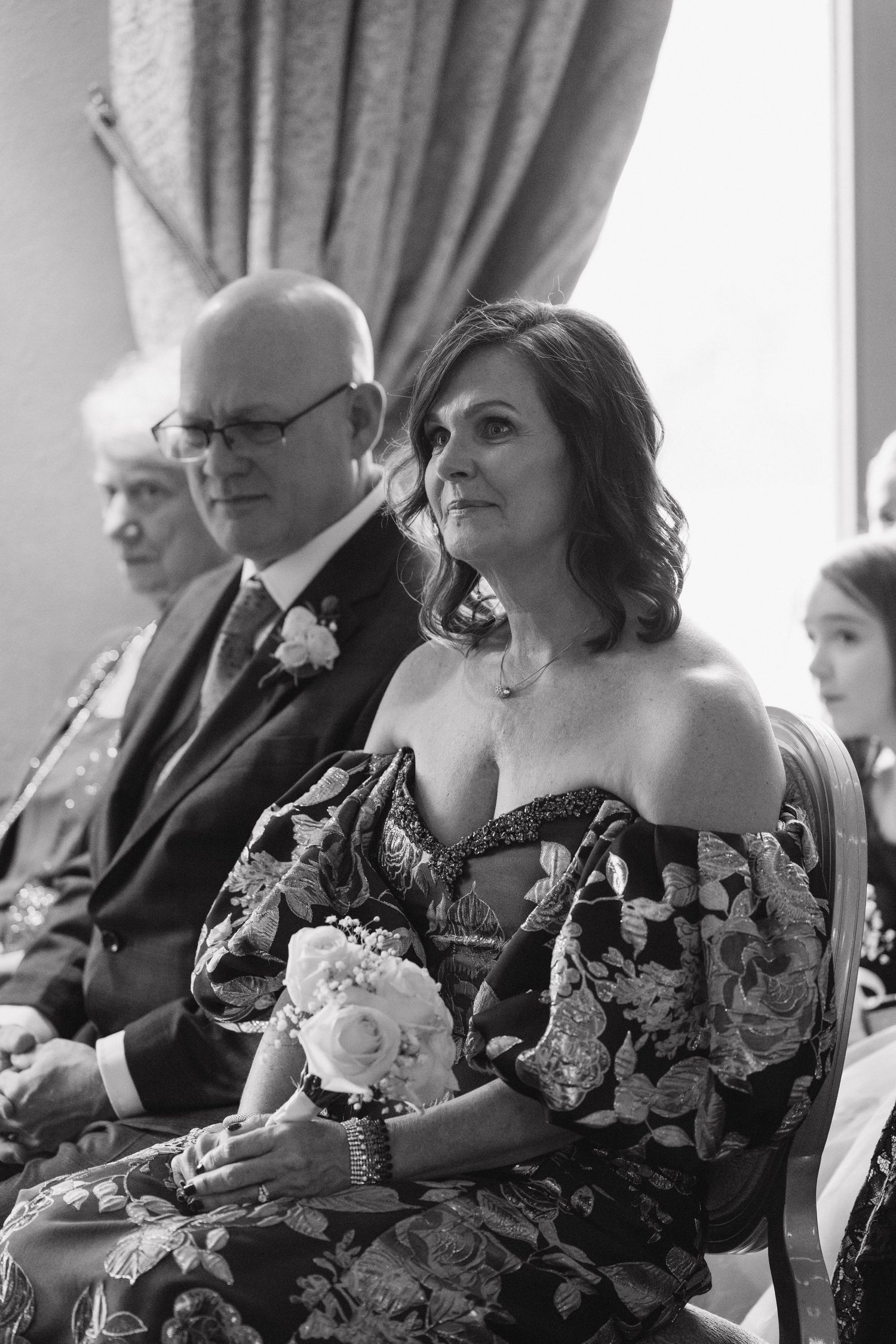 Wedding guests in formal attire seated in a row during a ceremony.