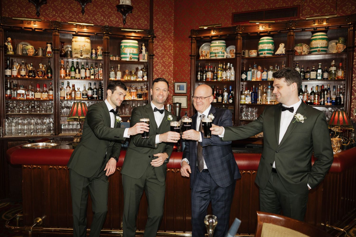 Groomsmen celebrating at vintage bar with dark wood and patterned wallpaper.