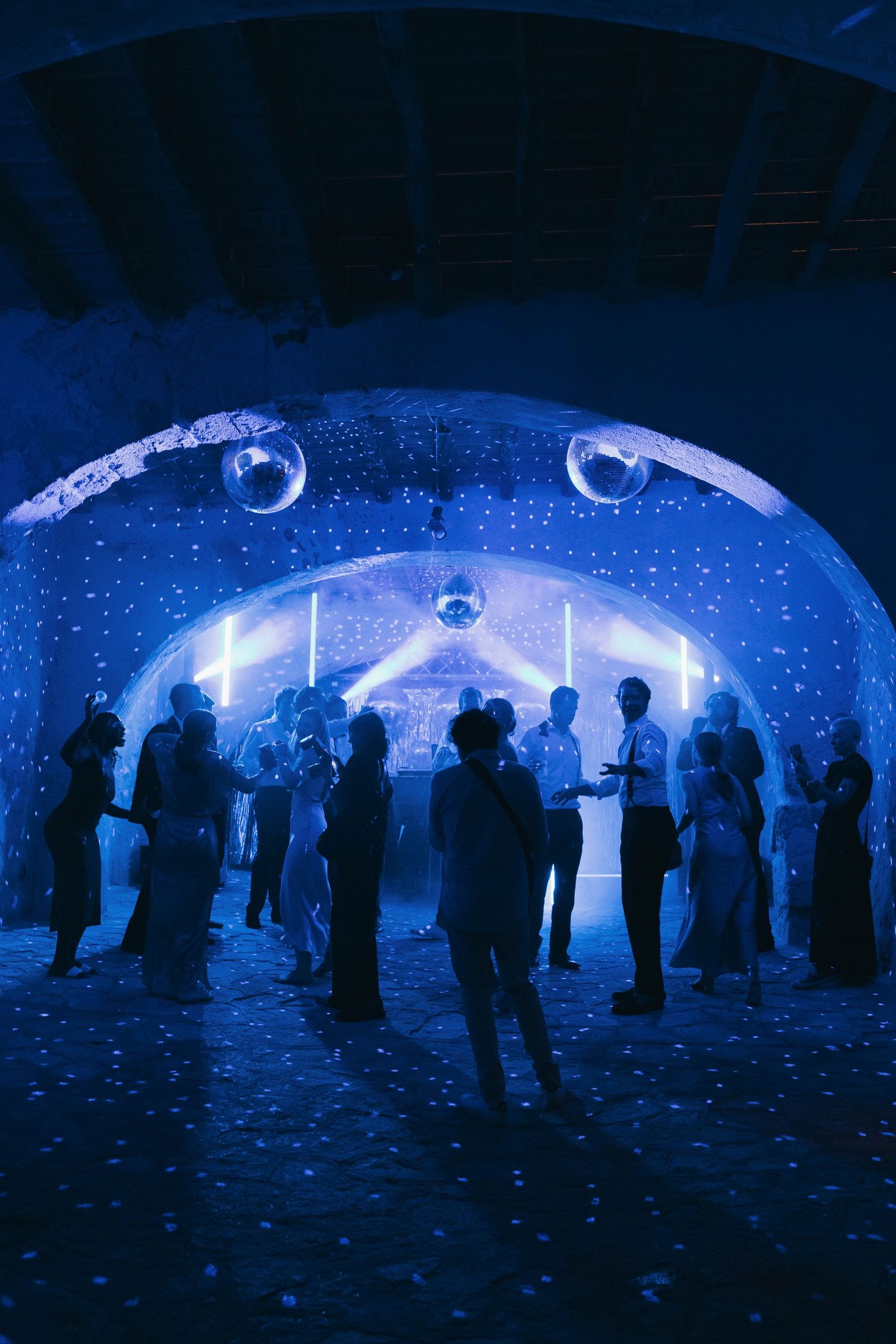 Silhouettes of people gathered in a dark blue illuminated dome-like space creating an ethereal atmosphere.