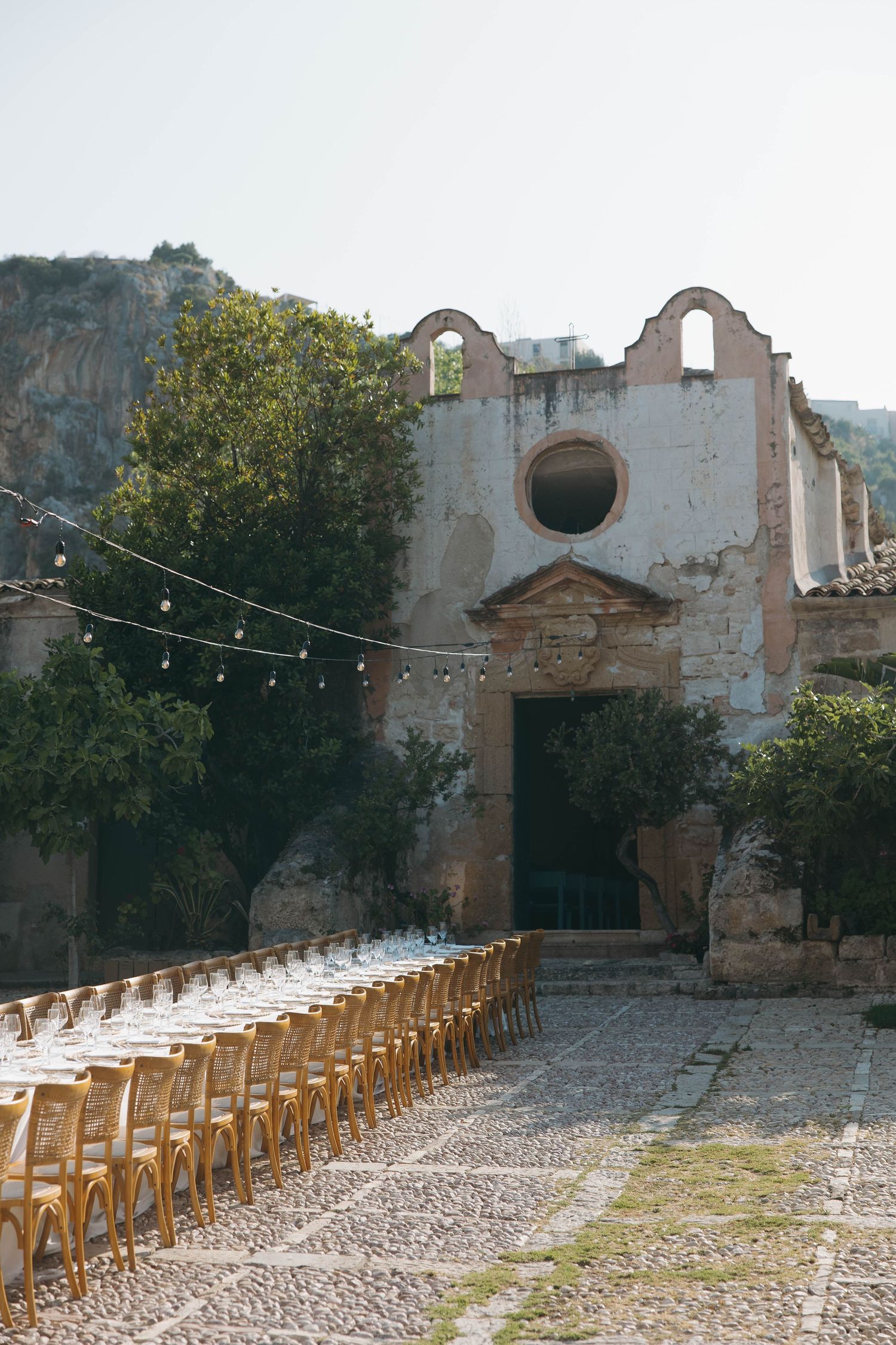 Historic stone courtyard set up for a wedding reception with wooden chairs and string lights.