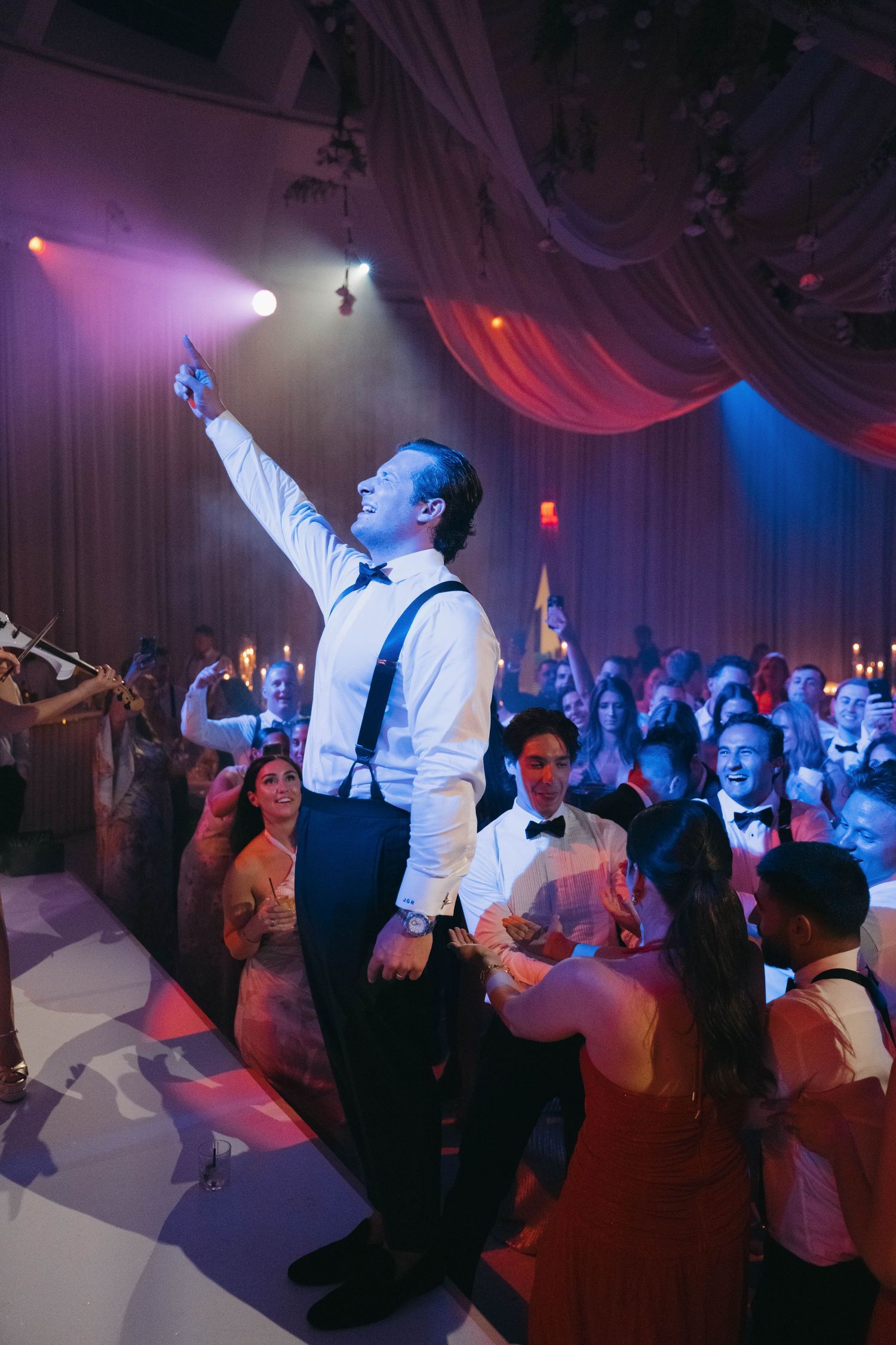 Wedding celebration with energetic dancing under purple and blue lighting.