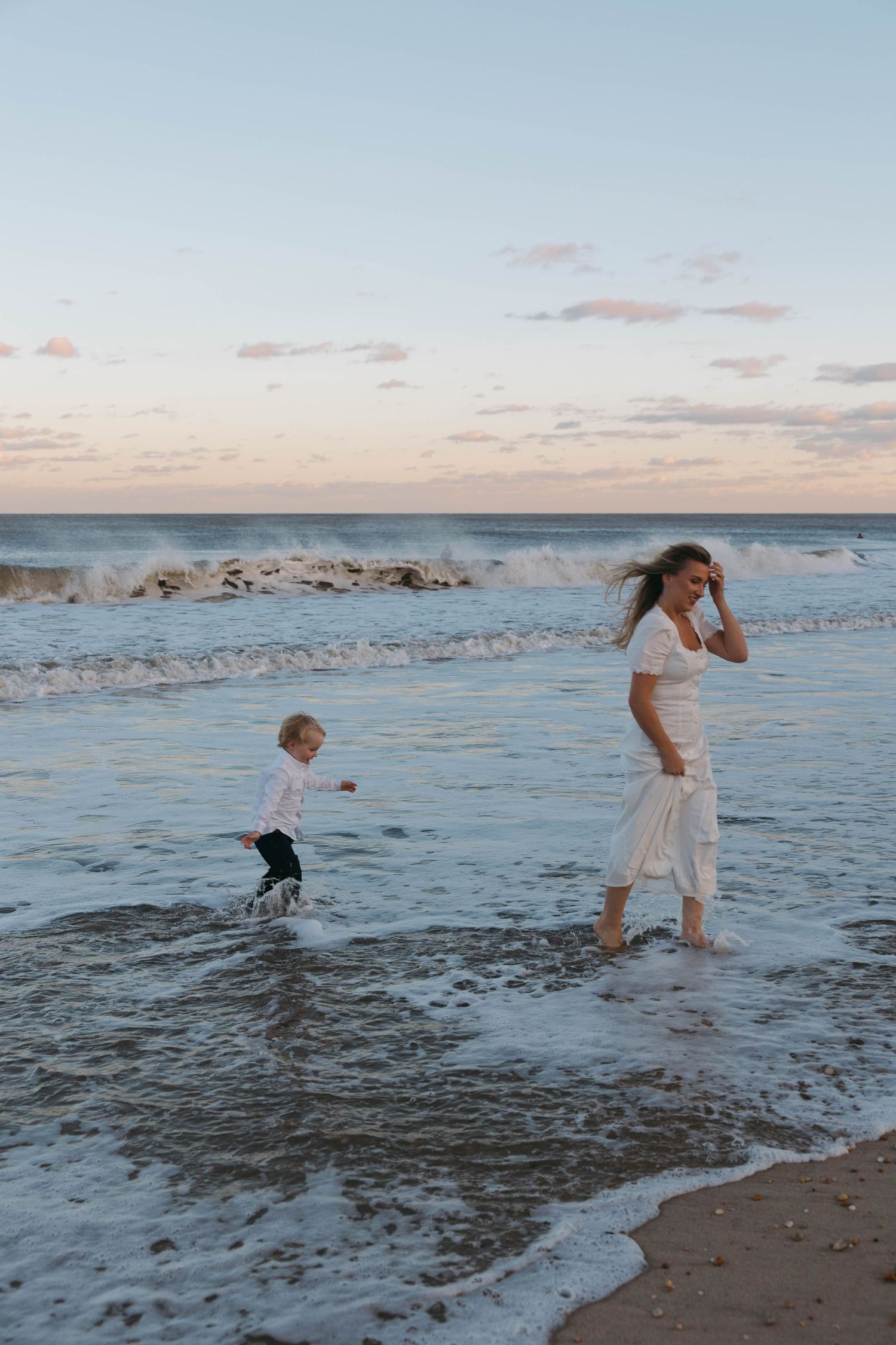 Two people splashing and playing in the ocean waves at sunset on a peaceful beach.
