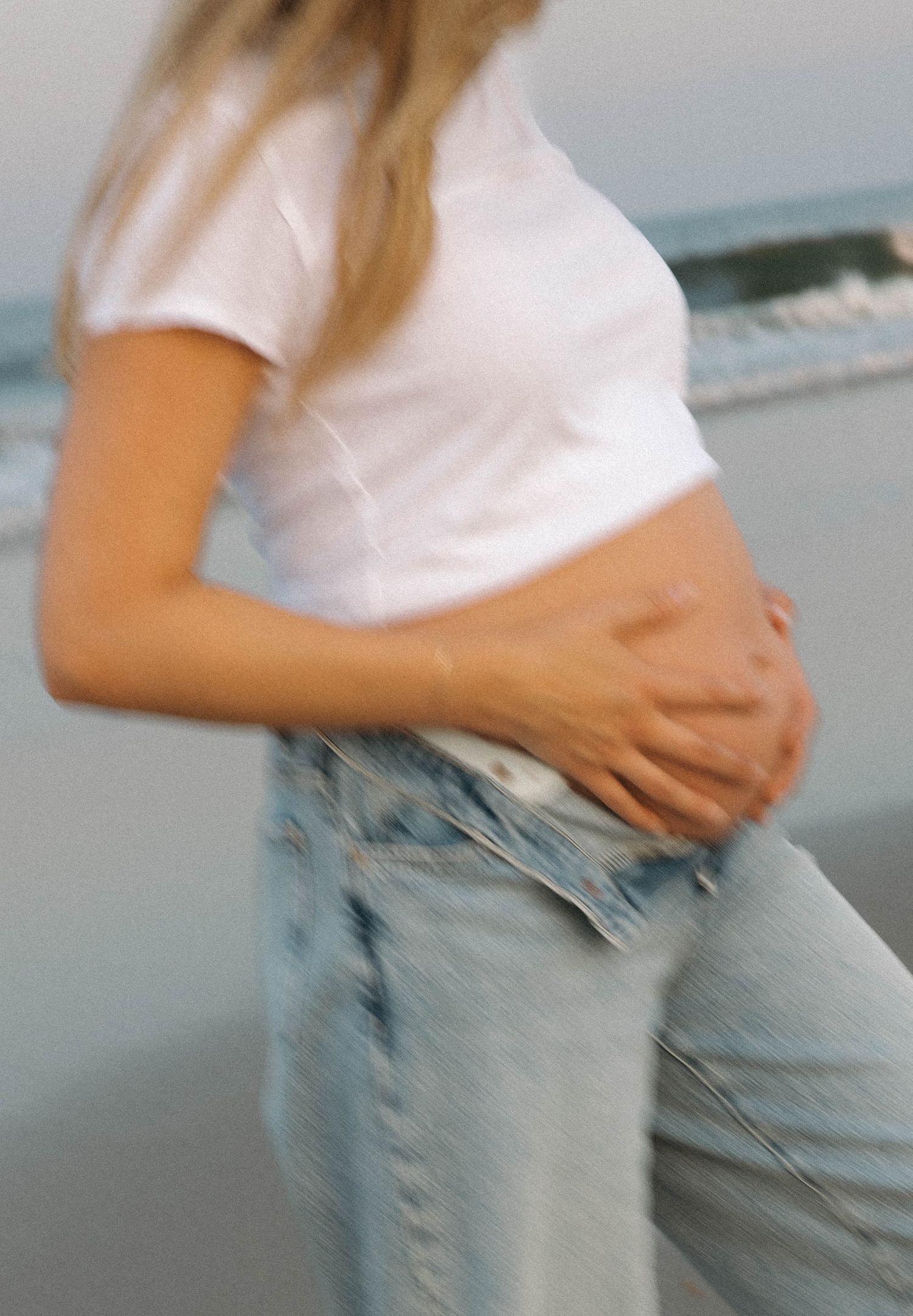 Motion-blurred image of someone in white top and jeans standing against a beach backdrop.