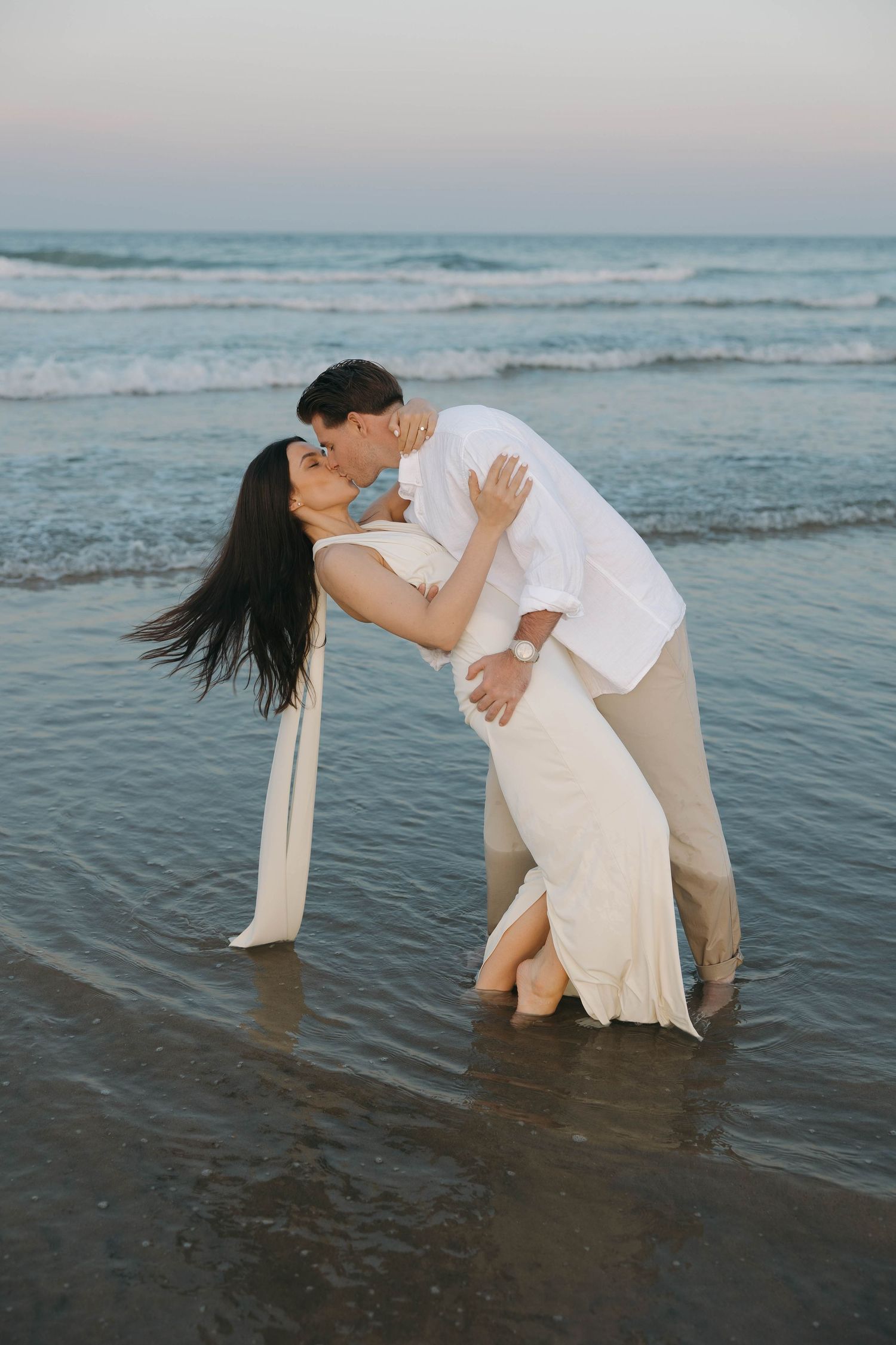 Romantic dance sequence of couple in white clothing on beach at sunset.