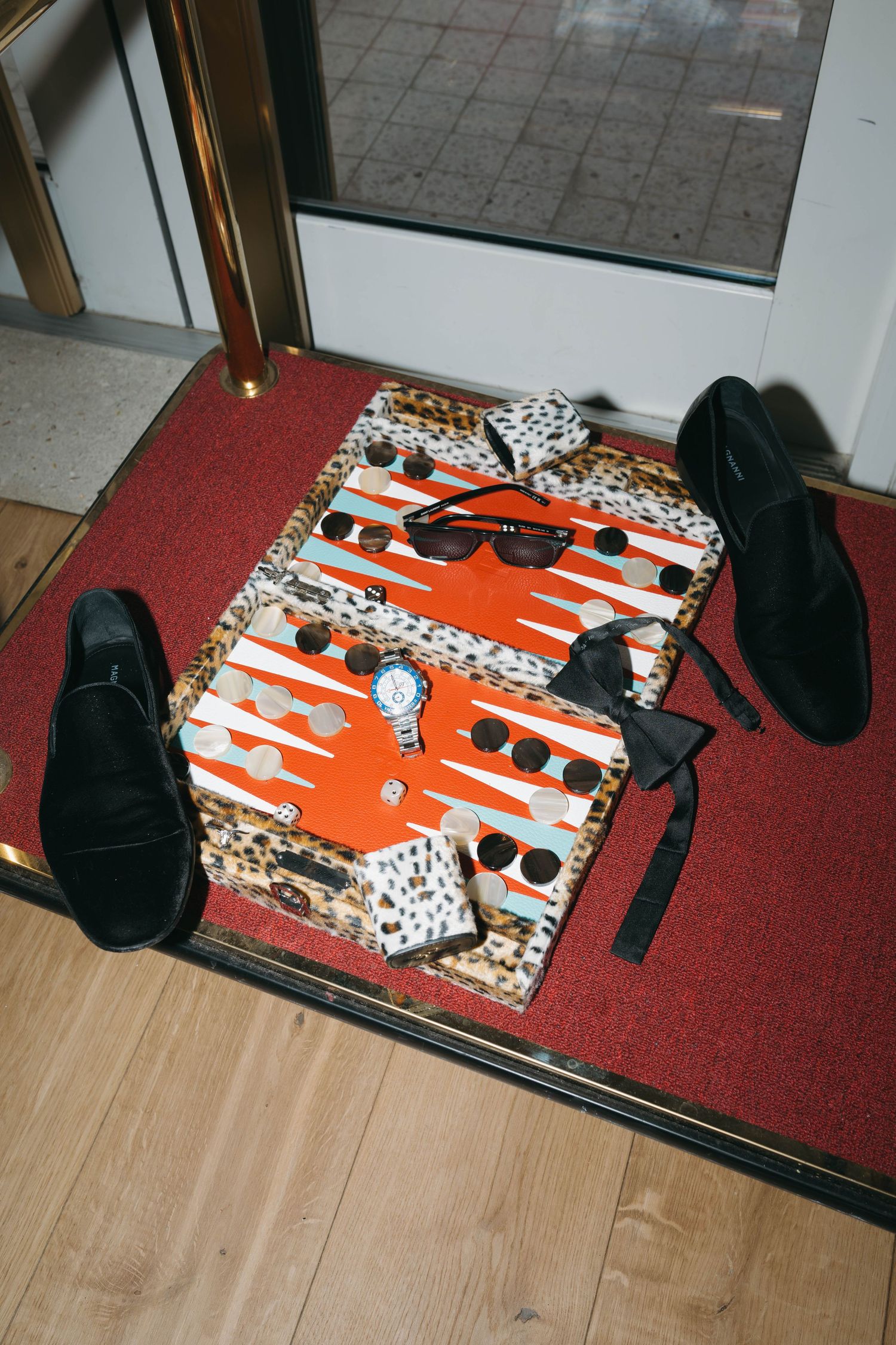 Orange and black patterned boxes with sunglasses and accessories laid out on a red carpet.
