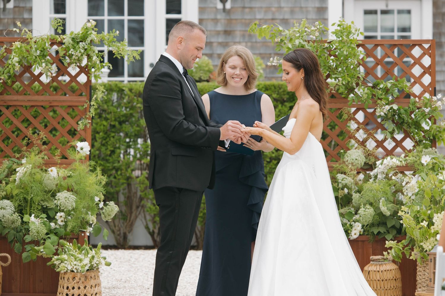 Wedding ceremony moment captured in front of lattice backdrop with floral arrangements.