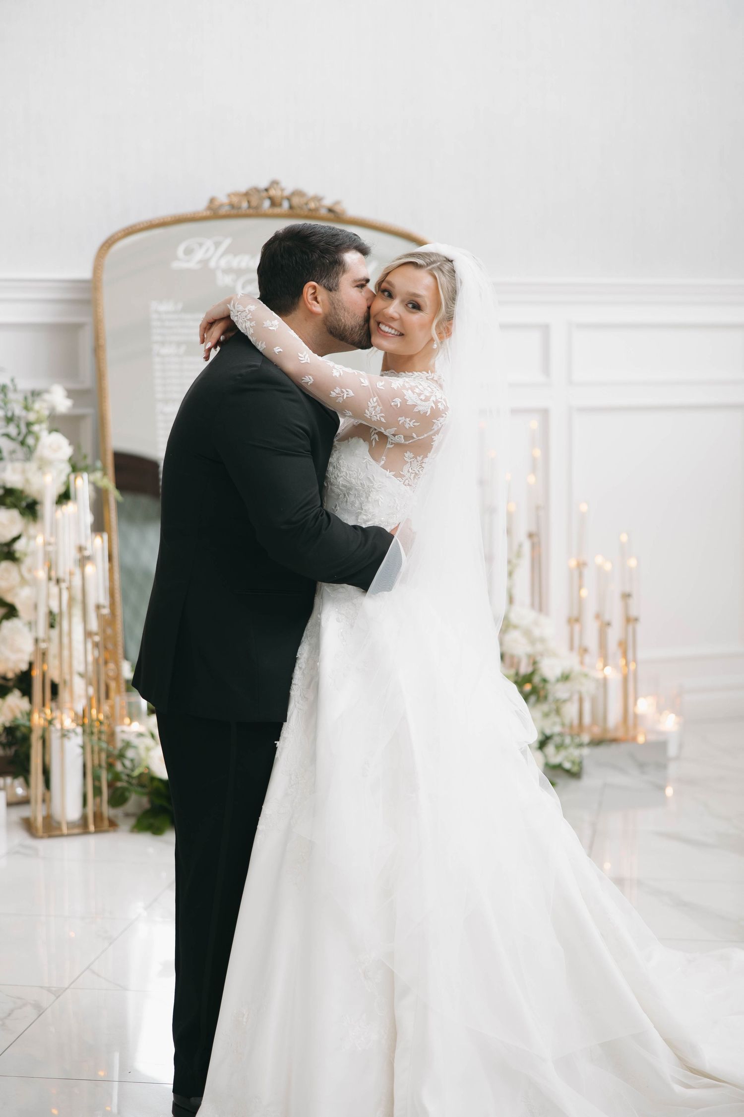Intimate wedding moment captured in an elegant white room with decorative mirrors.