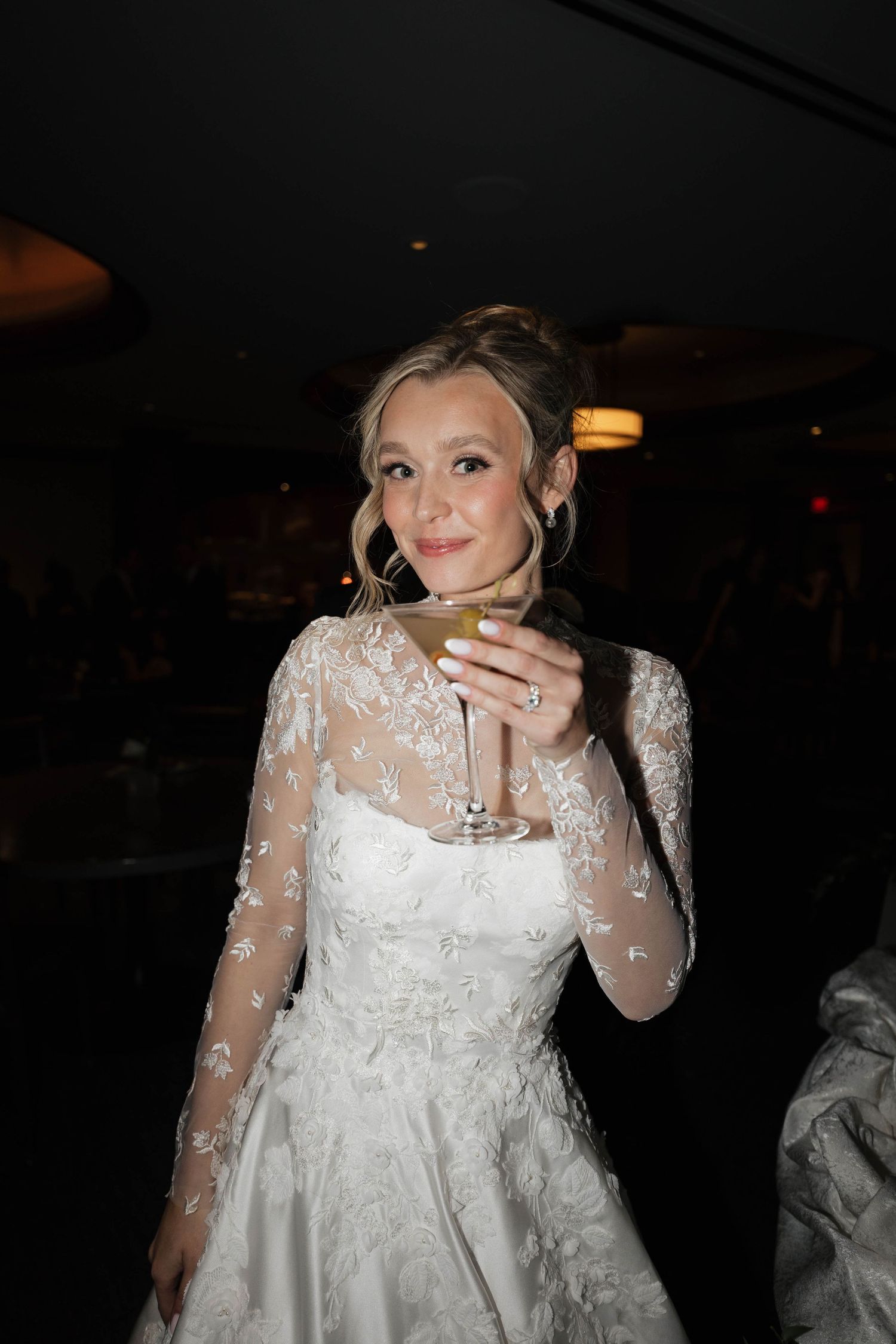 A person in an elegant white lace wedding dress poses during an evening celebration.
