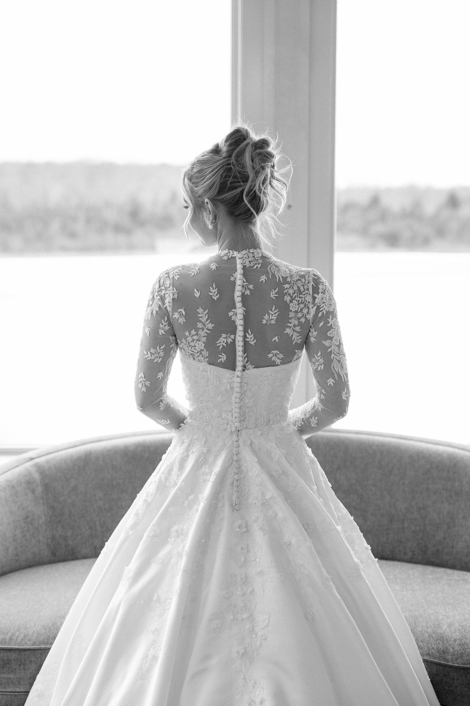 Back view of wedding gown featuring sheer lace bodice and full skirt against window backdrop.
