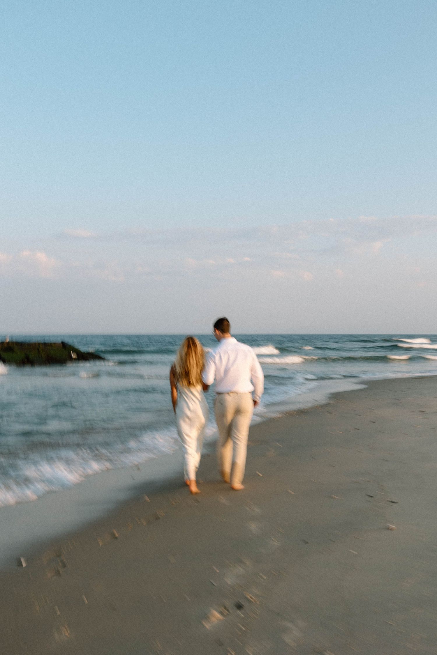 A couple walking hand in hand along the shoreline at sunset.