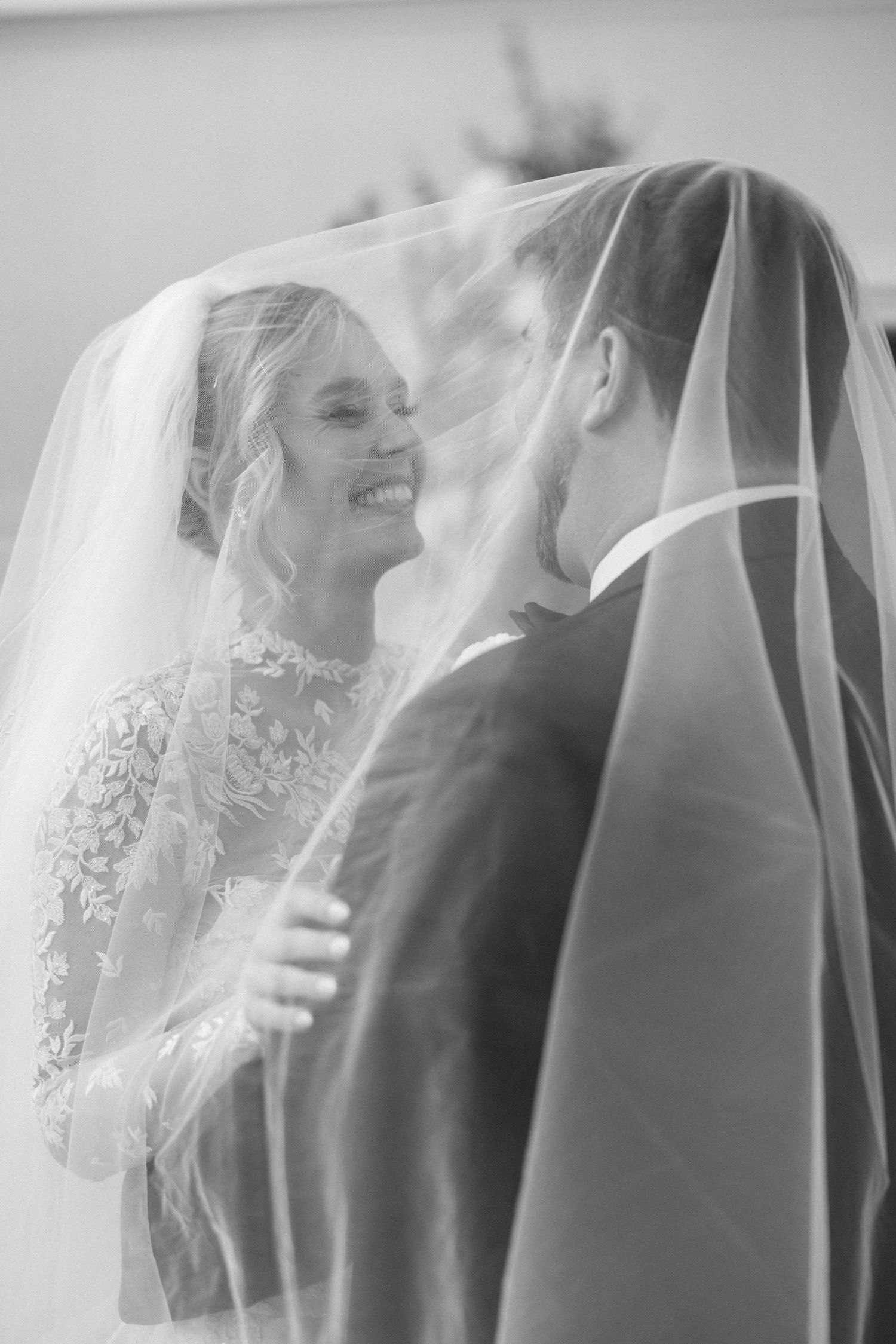 Ethereal black and white portraits of couple beneath sheer wedding veil.