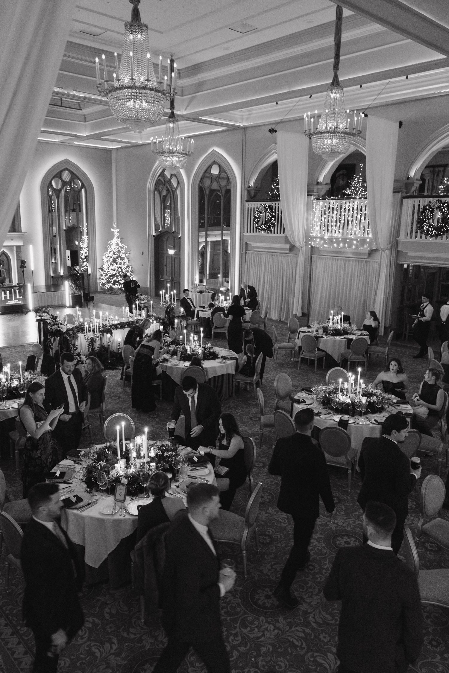 Wide shot of an elegant ballroom reception with guests seated at round tables under crystal chandeliers.