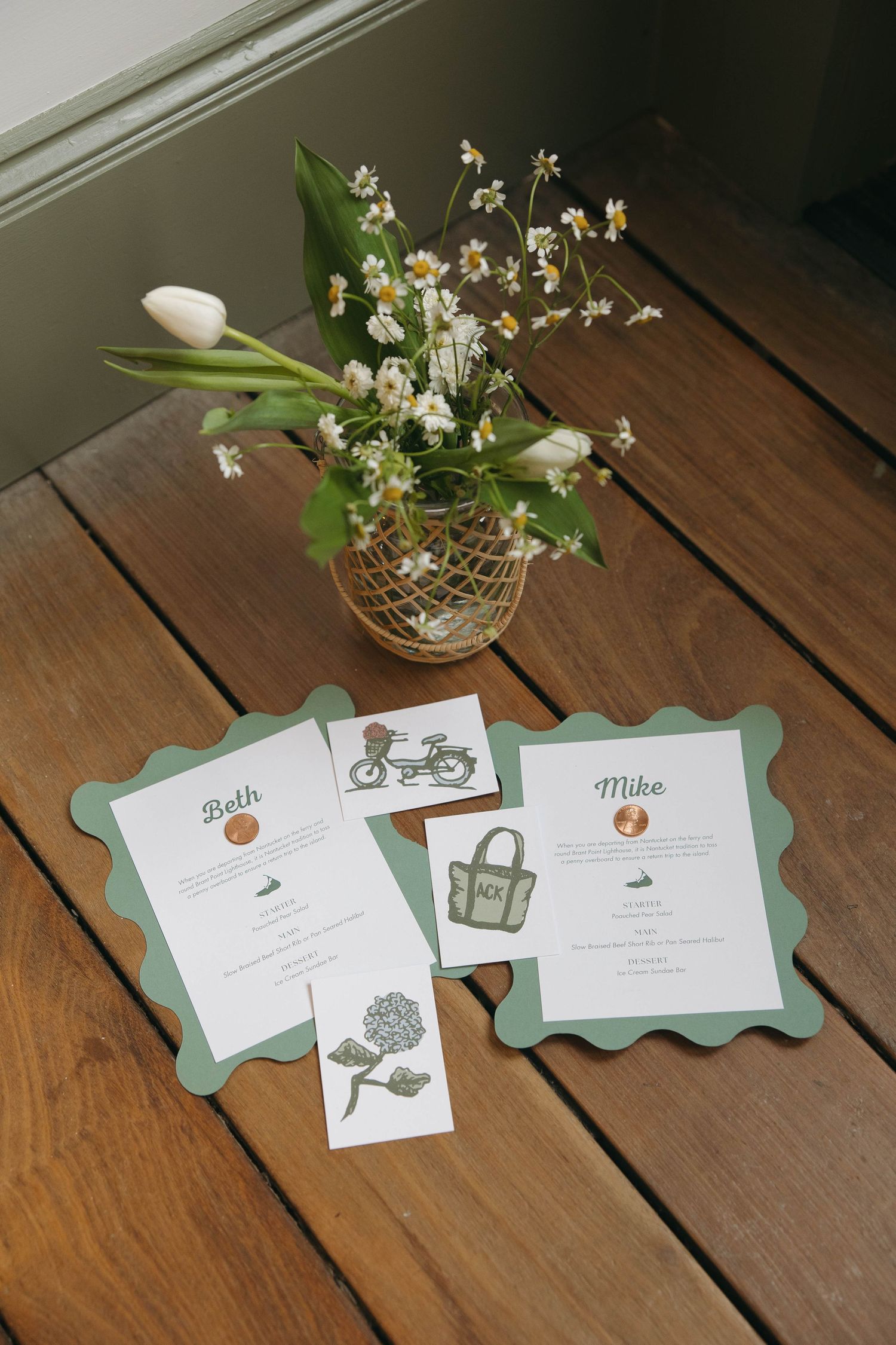 Wedding invitation cards and floral centerpiece with white flowers displayed on wooden table.