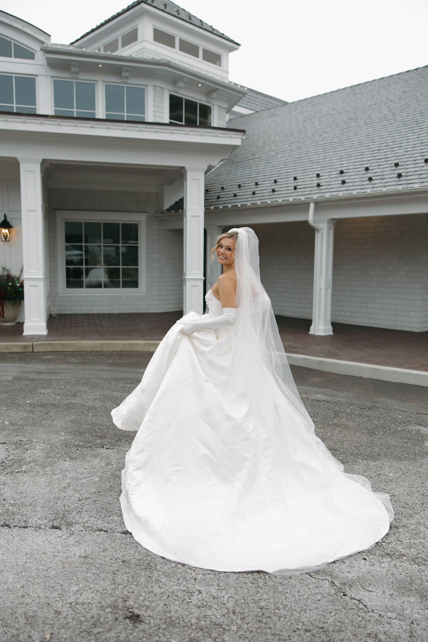 A dramatic bridal portrait showcases the full skirt of a white wedding gown against stone ground.